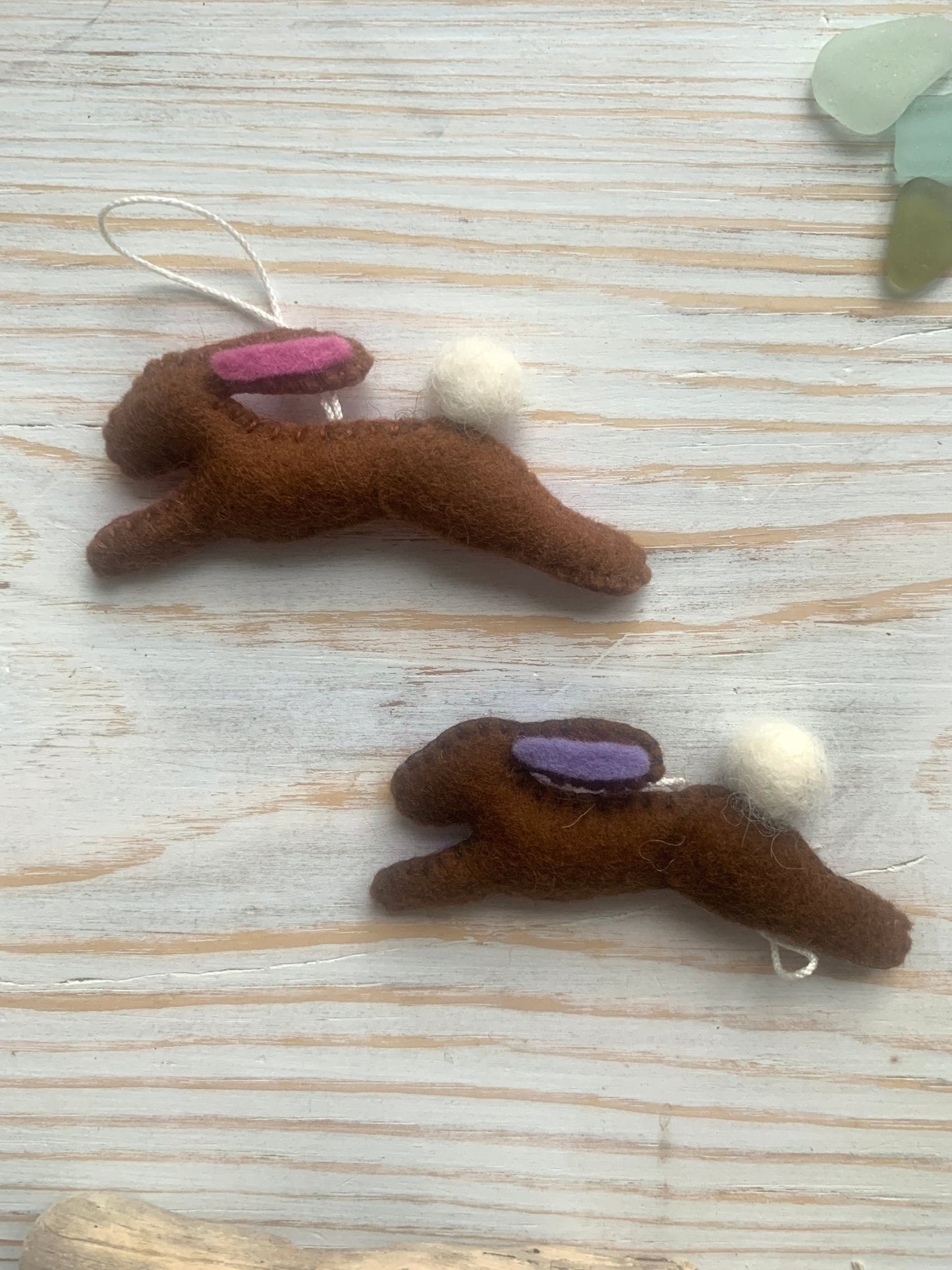 two handmade brown felt Easter bunny decorations in a leaping position with pink/lilac ear lining spring rabbit ornaments with fluffy pom-pom tails easter decor gift