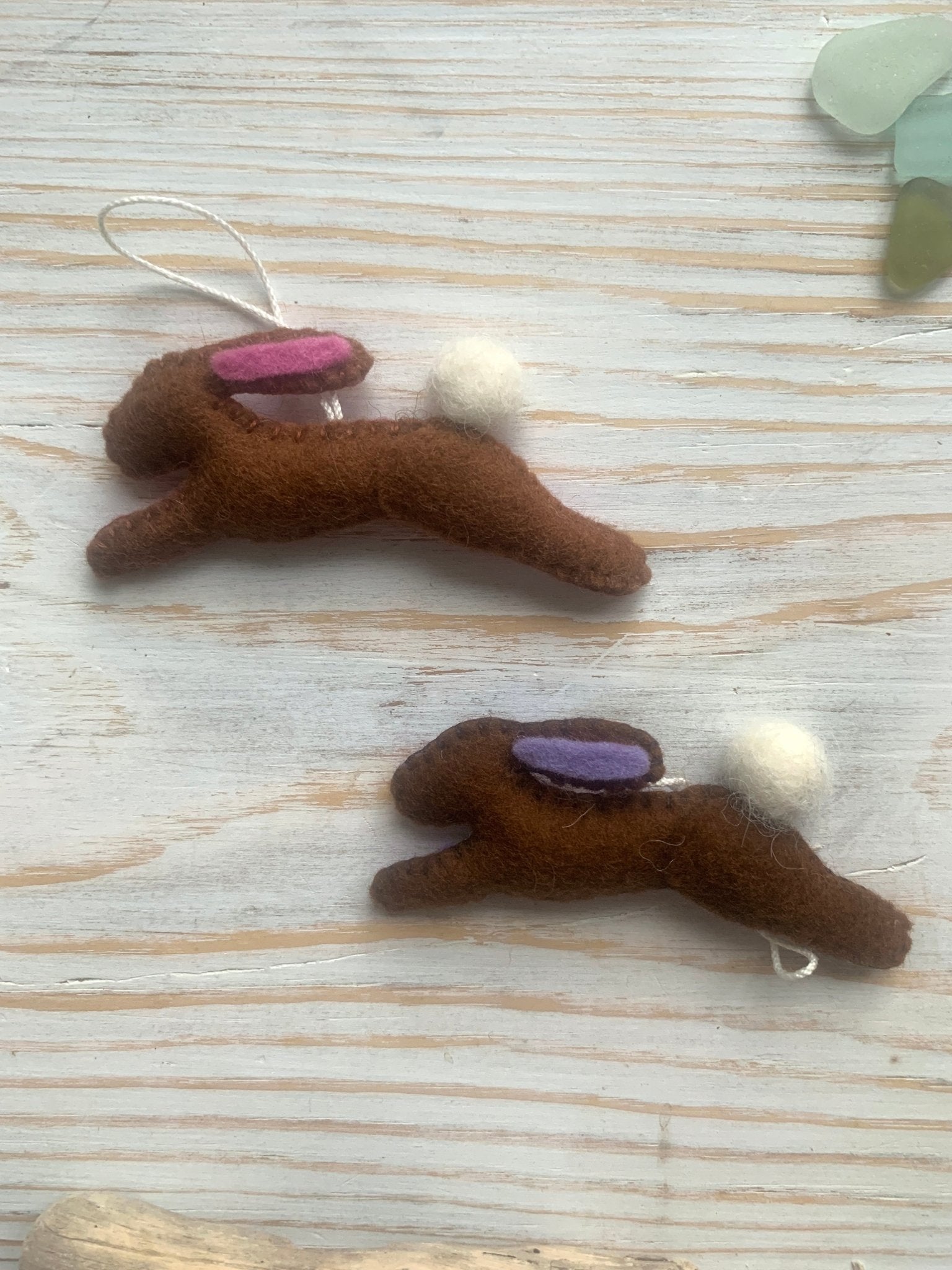 two handmade brown felt Easter bunny decorations in a leaping position with pink/lilac ear lining spring rabbit ornaments with fluffy pom-pom tails easter decor gift