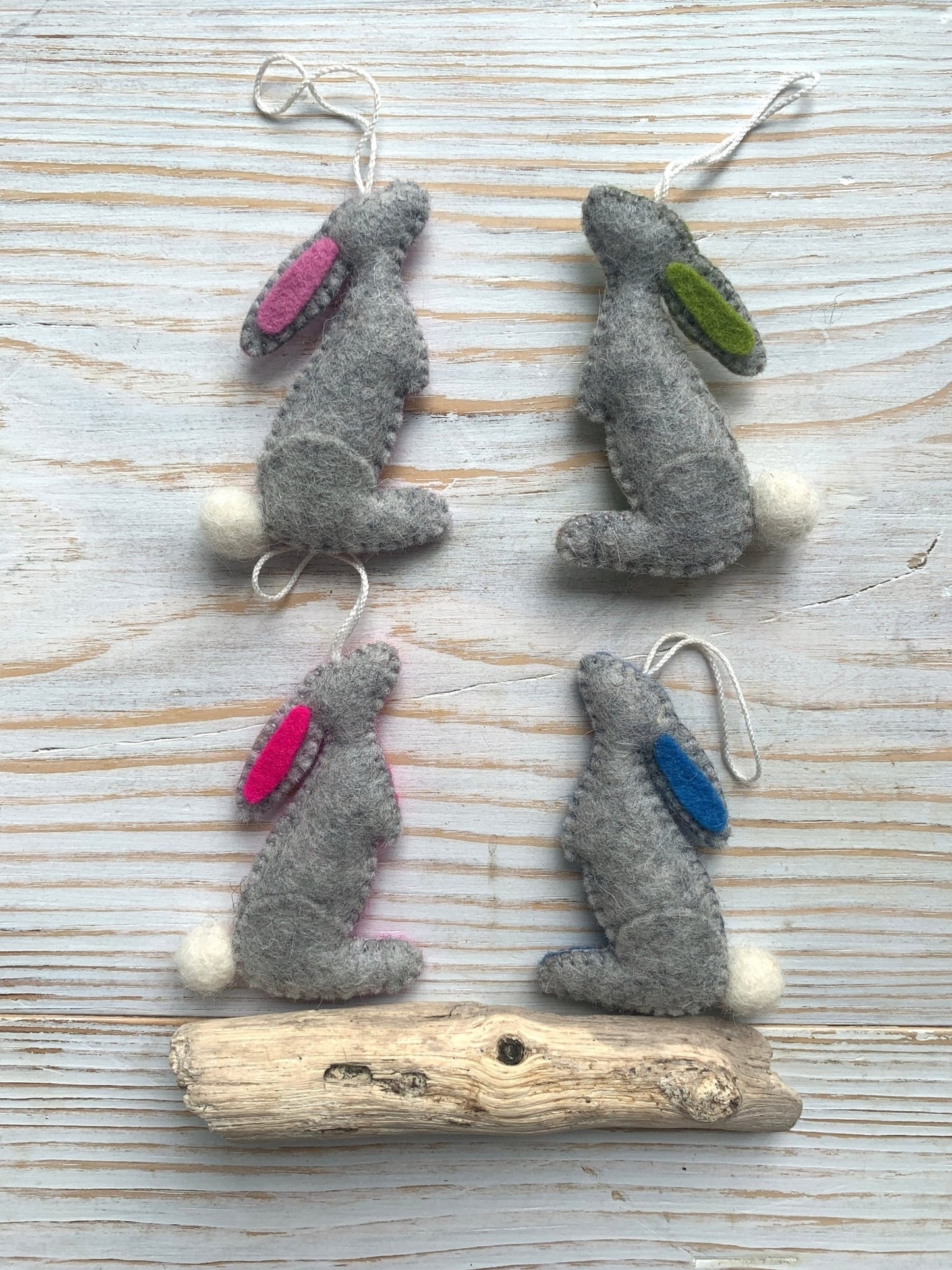 four handmade grey felt Easter bunny decorations in a stargazing pose with colored ear linings spring rabbit ornaments with fluffy tails easter decor gift