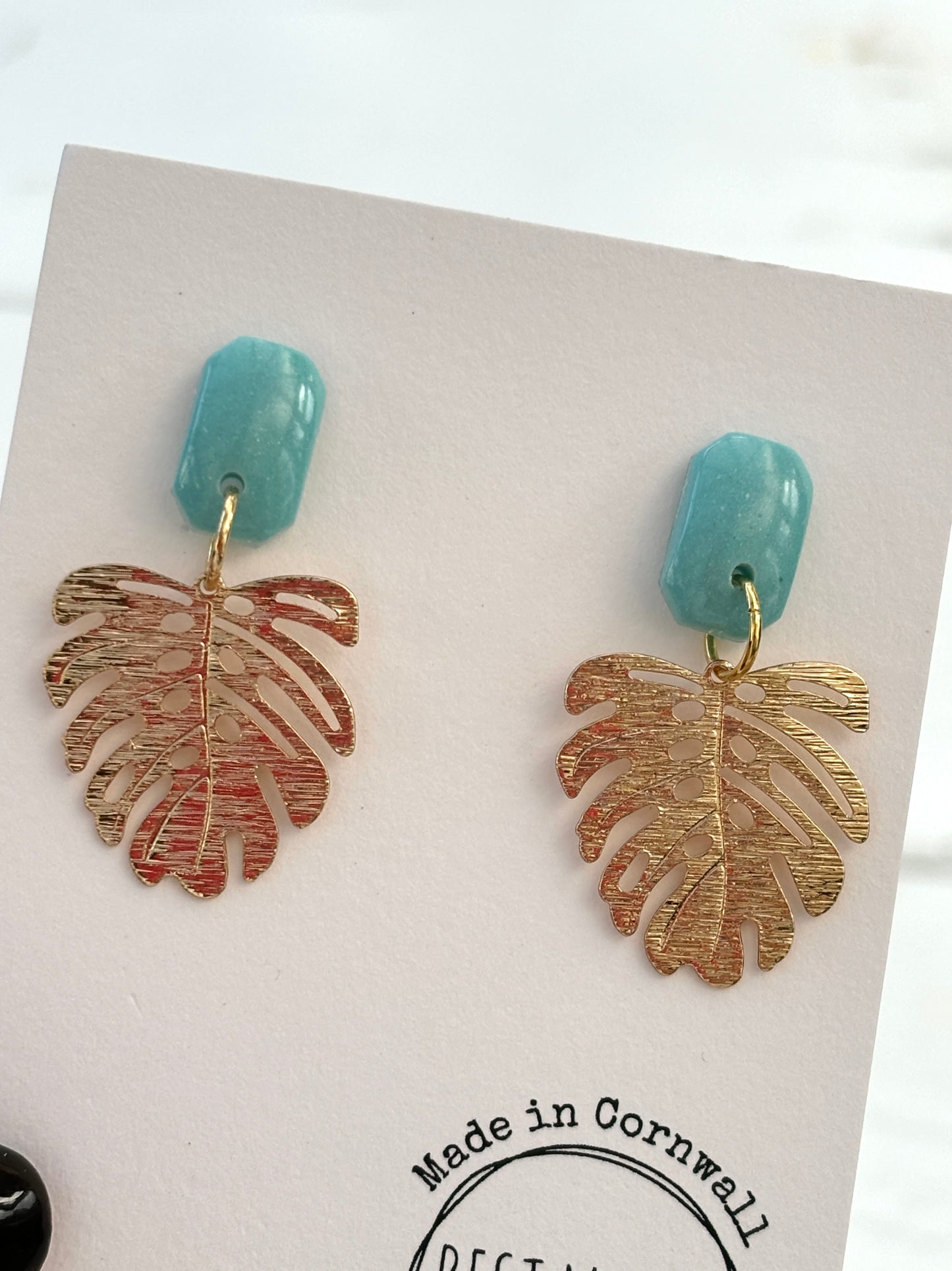 closeup shot of handmade Monstera earrings—light blue stud with gold leaf charm, tropical botanical gift from Cornwall