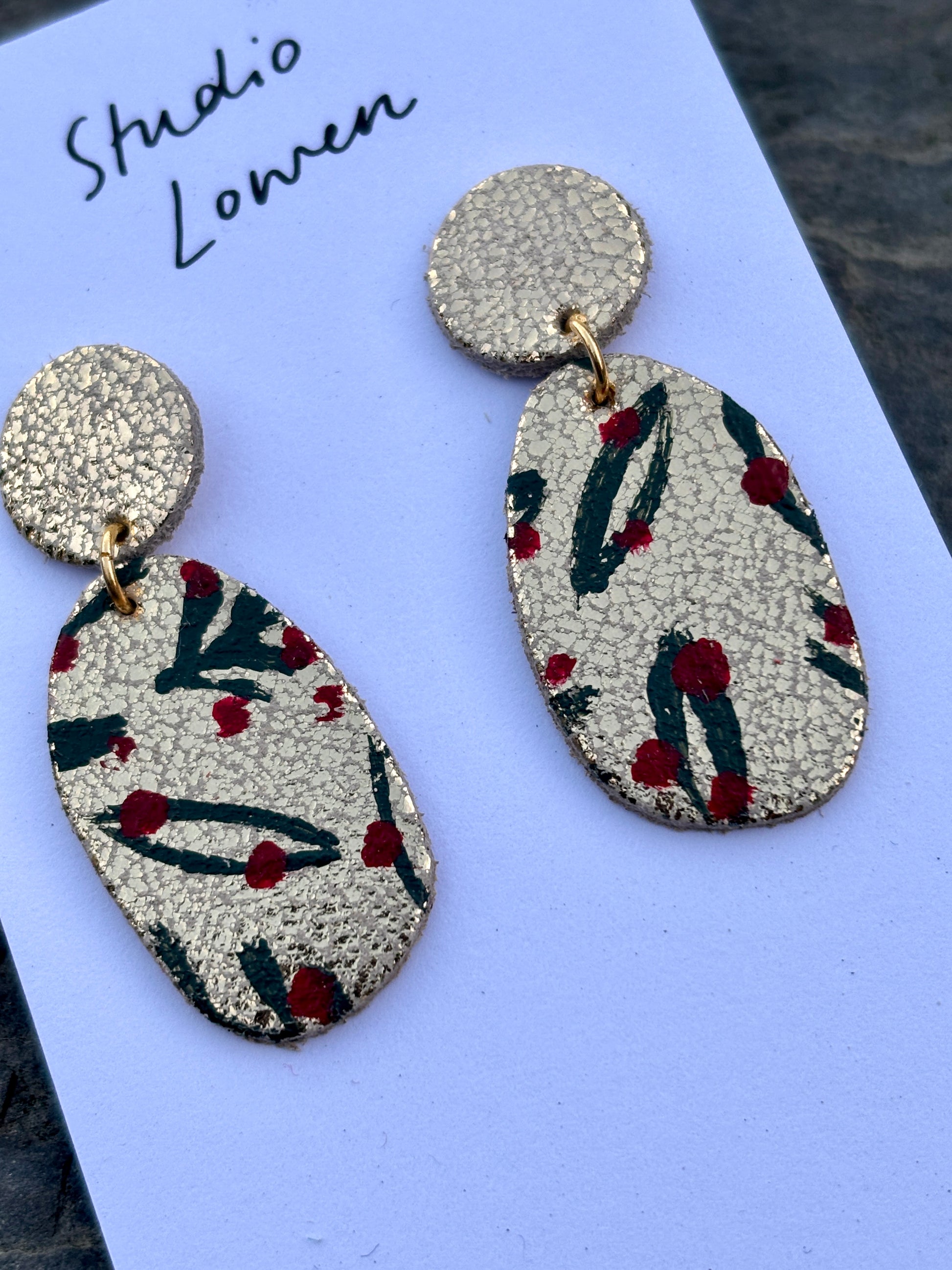 closeup shot of hand-painted gold drop earrings—festive leaf motif, artisan-crafted with red accents for bold holiday styling