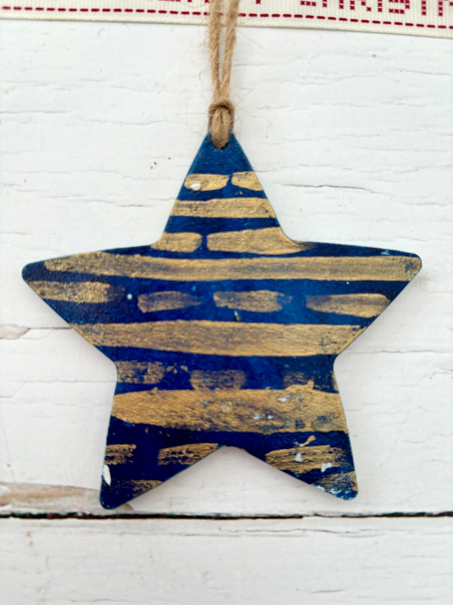closeup shot of a hand-painted wooden star decoration in navy blue with distressed gold metallic stripes nautical Christmas ornament with a rustic finish