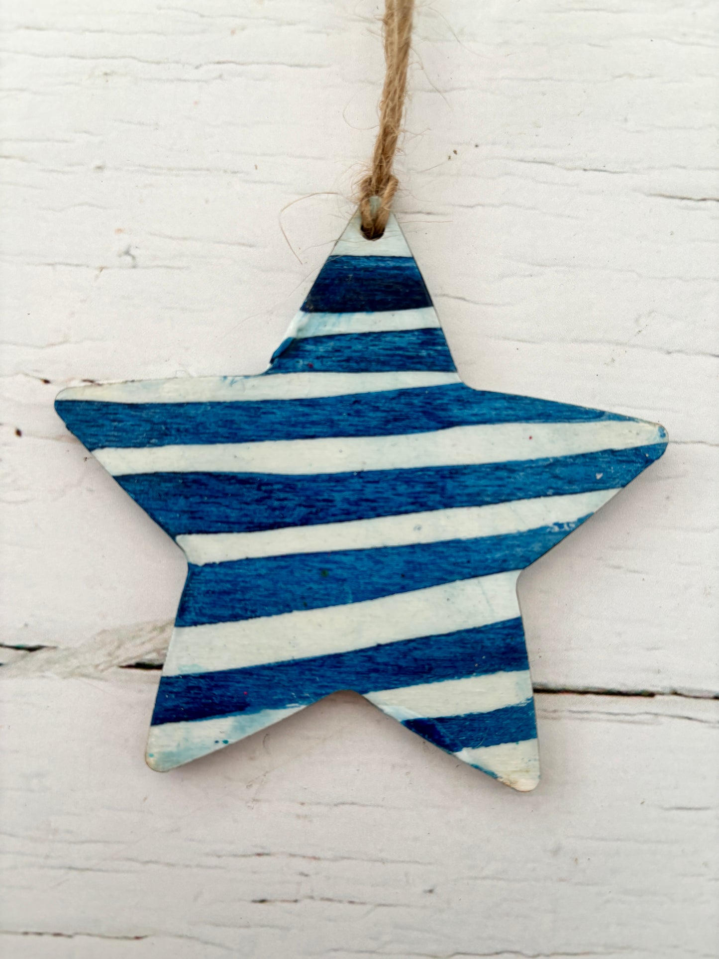 closeup shot of a hand-painted wooden star decoration in blue with bold white nautical stripes coastal Christmas ornament with a distressed rustic finish