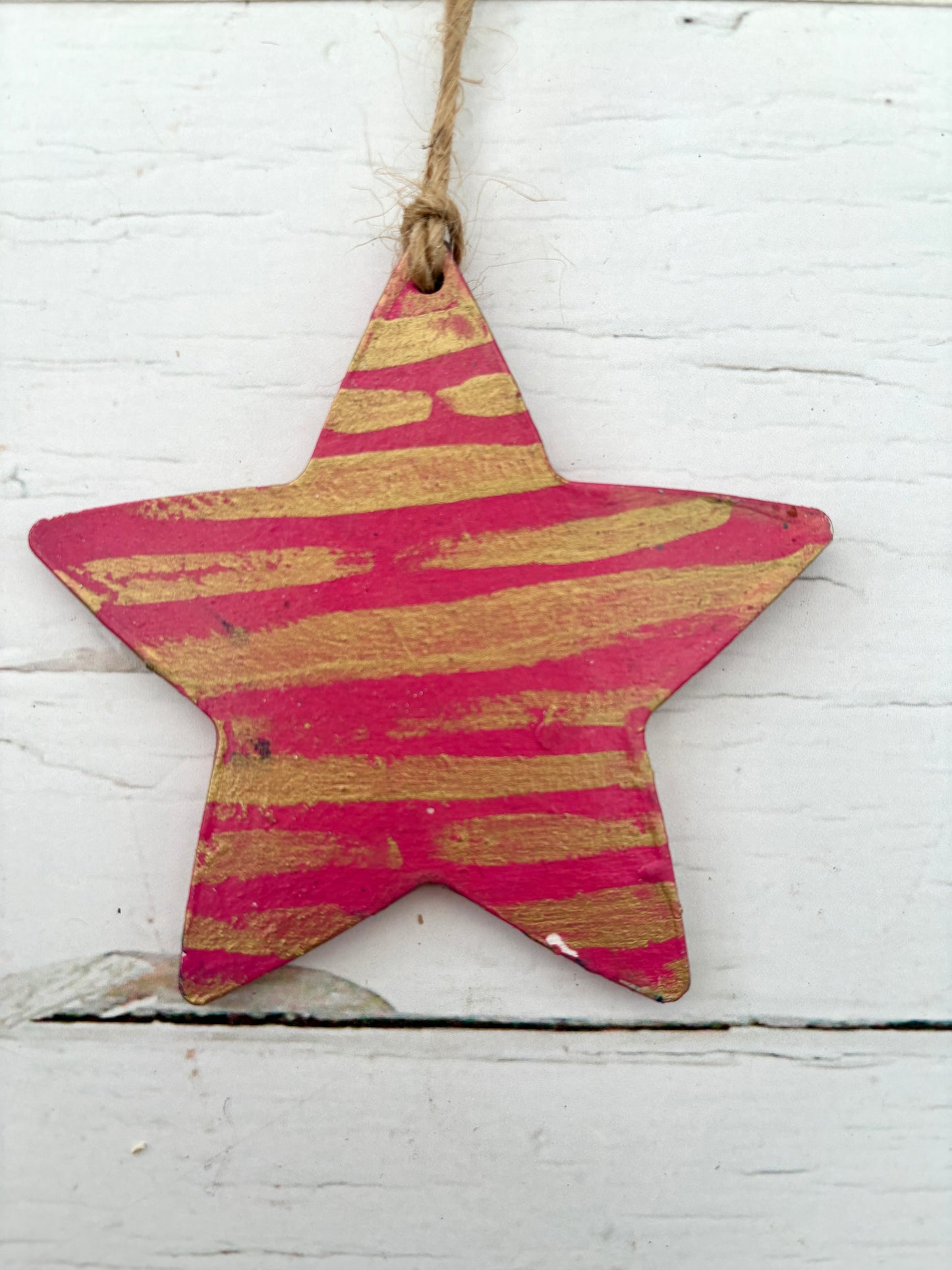 closeup shot of a hand-painted wooden star decoration in bright pink with distressed gold stripes coastal Christmas ornament with a rustic, metallic finish