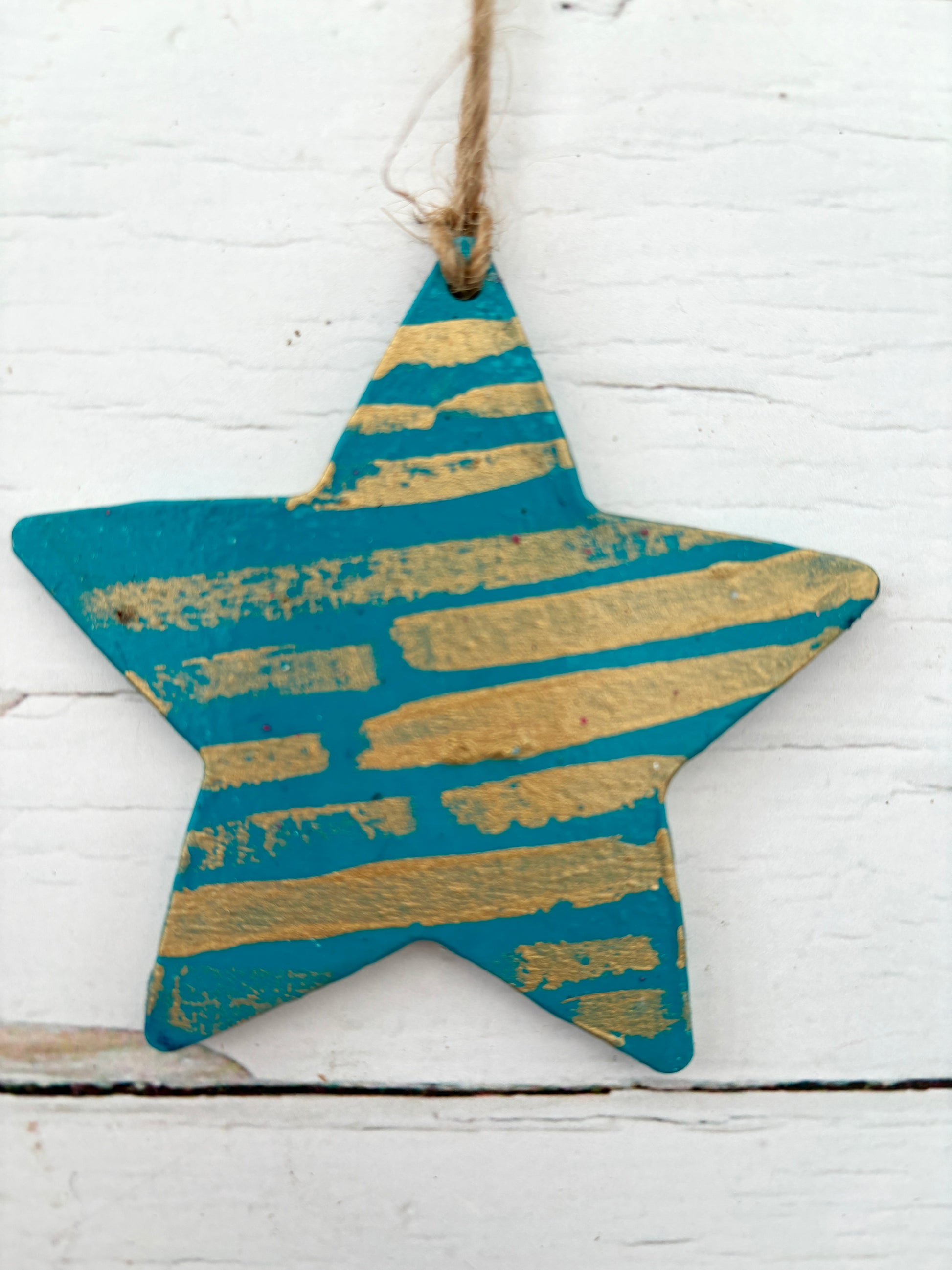 closeup shot of a hand-painted wooden star decoration in teal with distressed gold stripes coastal Christmas ornament with a rustic, metallic finish