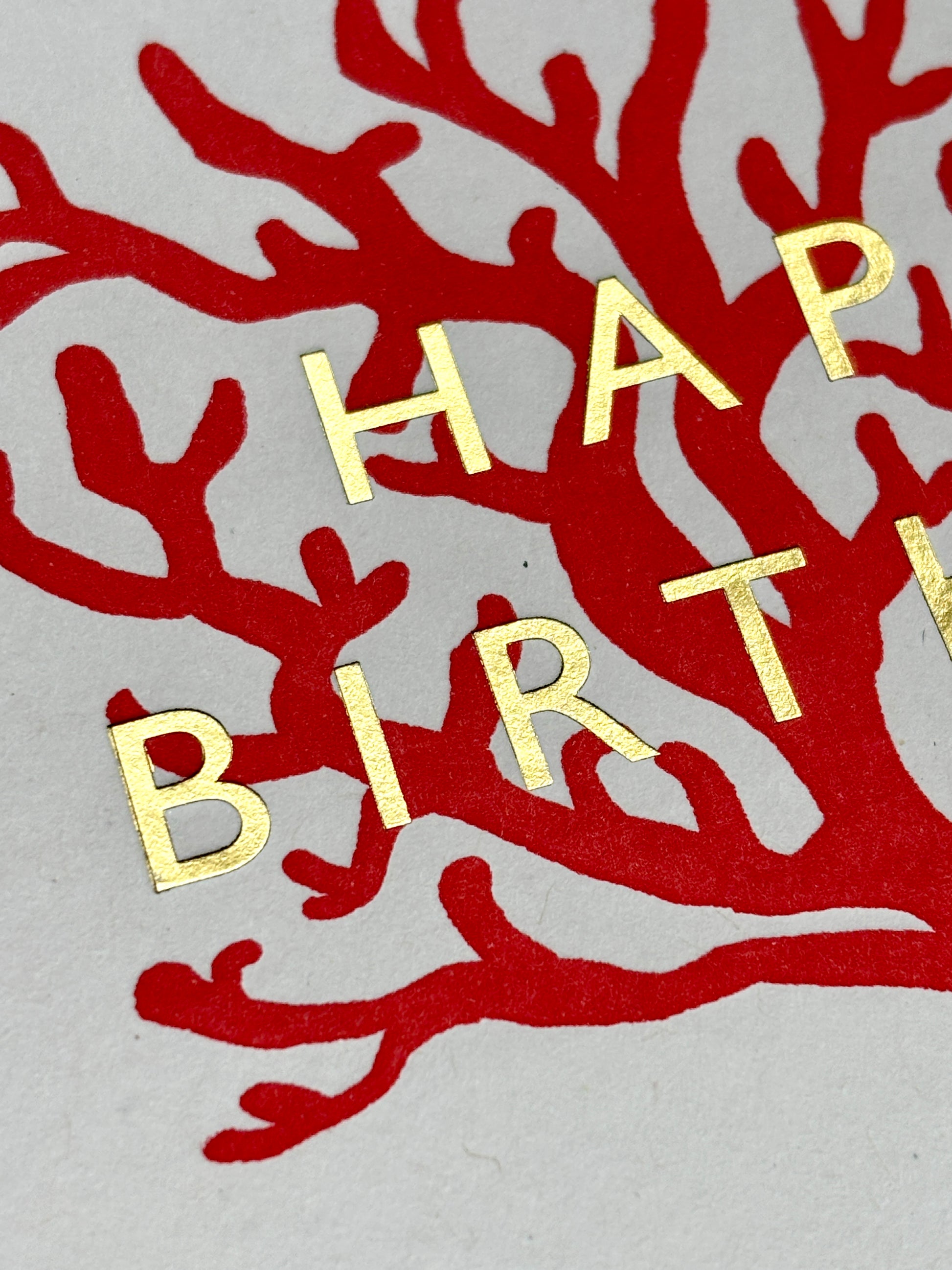 closeup shot of red coral birthday card with gold foil text, elegant ocean-inspired design for coastal gifting and celebrations
