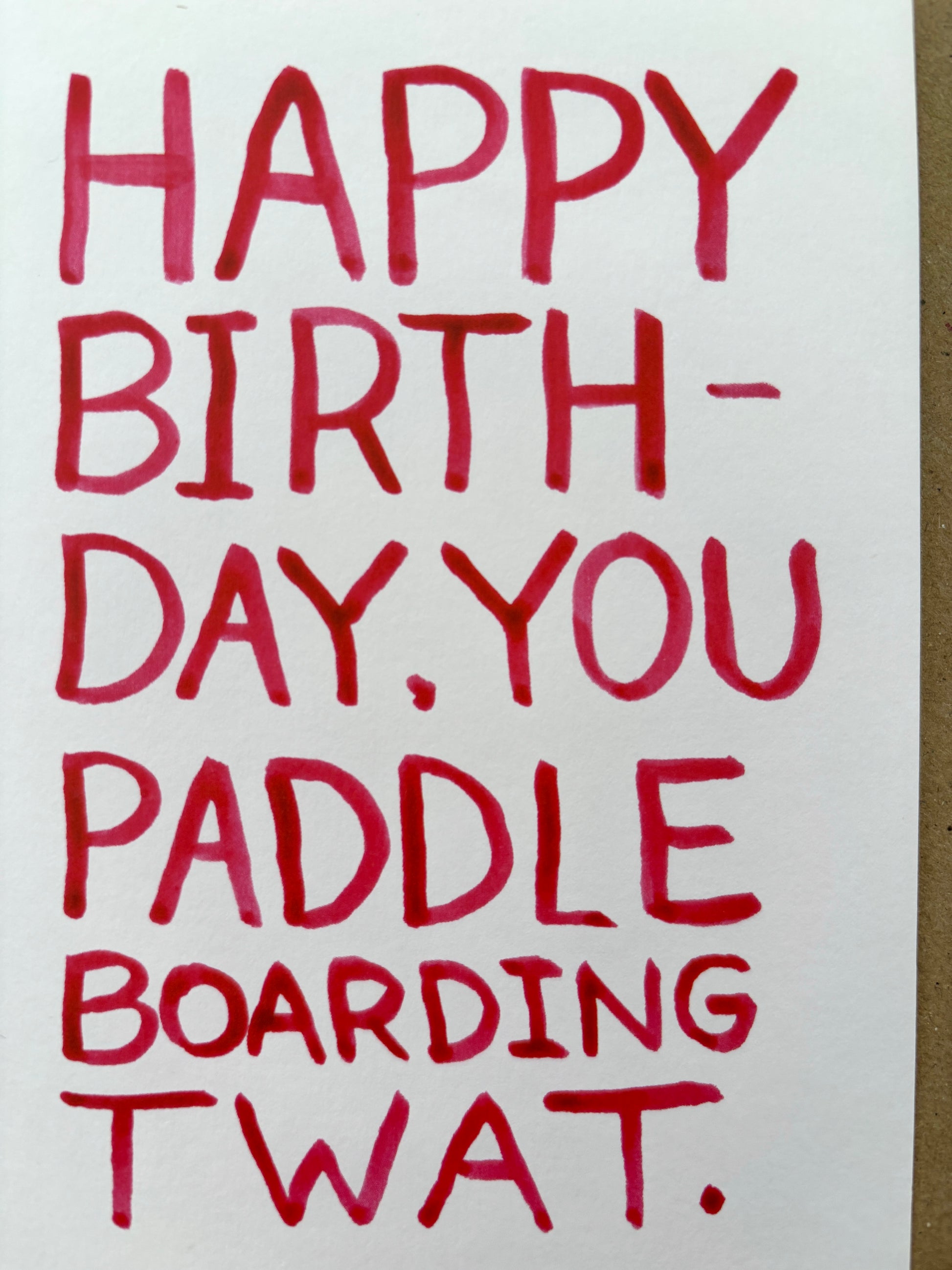 closeup shot of cheeky birthday card for paddleboarders—bold red sweary text, handmade coastal humor for close friends