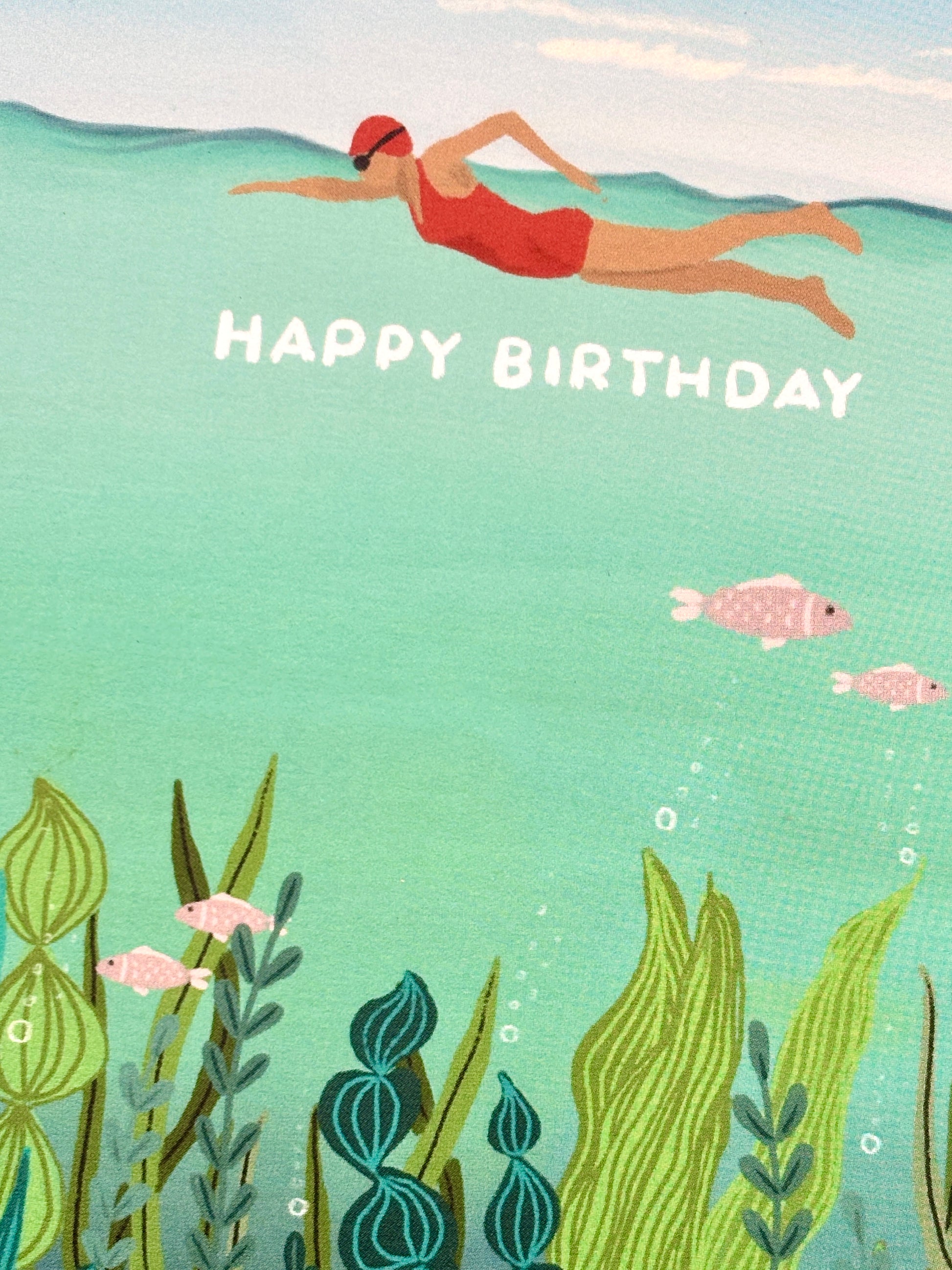 closeup shot of a Happy Birthday card showing an underwater illustration of a swimmer and colorful marine plants and pink fish coastal greeting card for sea swimmers