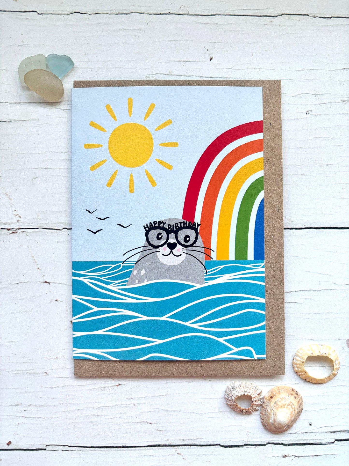 happy birthday seal card with rainbow, sunshine, ocean waves, cute illustrated seal wearing glasses coastal theme