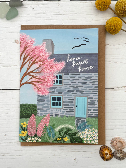 country cottage greeting card—illustrated stone house, blooming garden, “home sweet home” message, cozy coastal stationery
