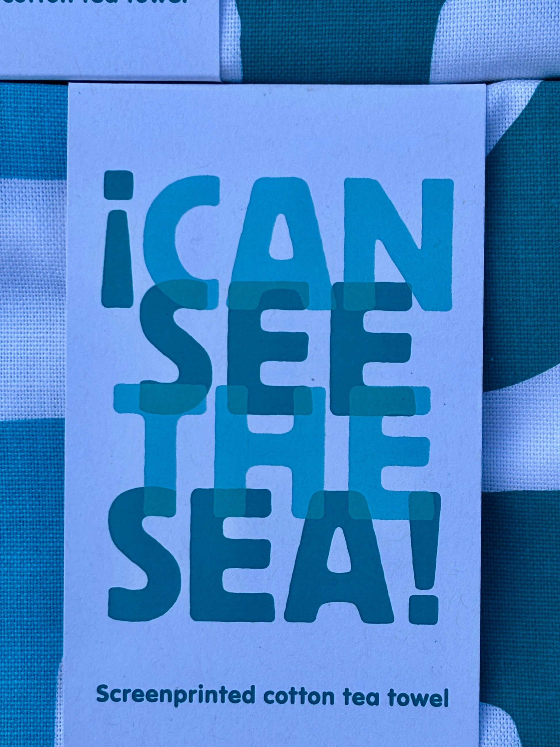 closeup shot of a "I Can See The Sea!" screenprinted cotton tea towel label abstract block design in teal and blue shades nautical kitchen linen detail