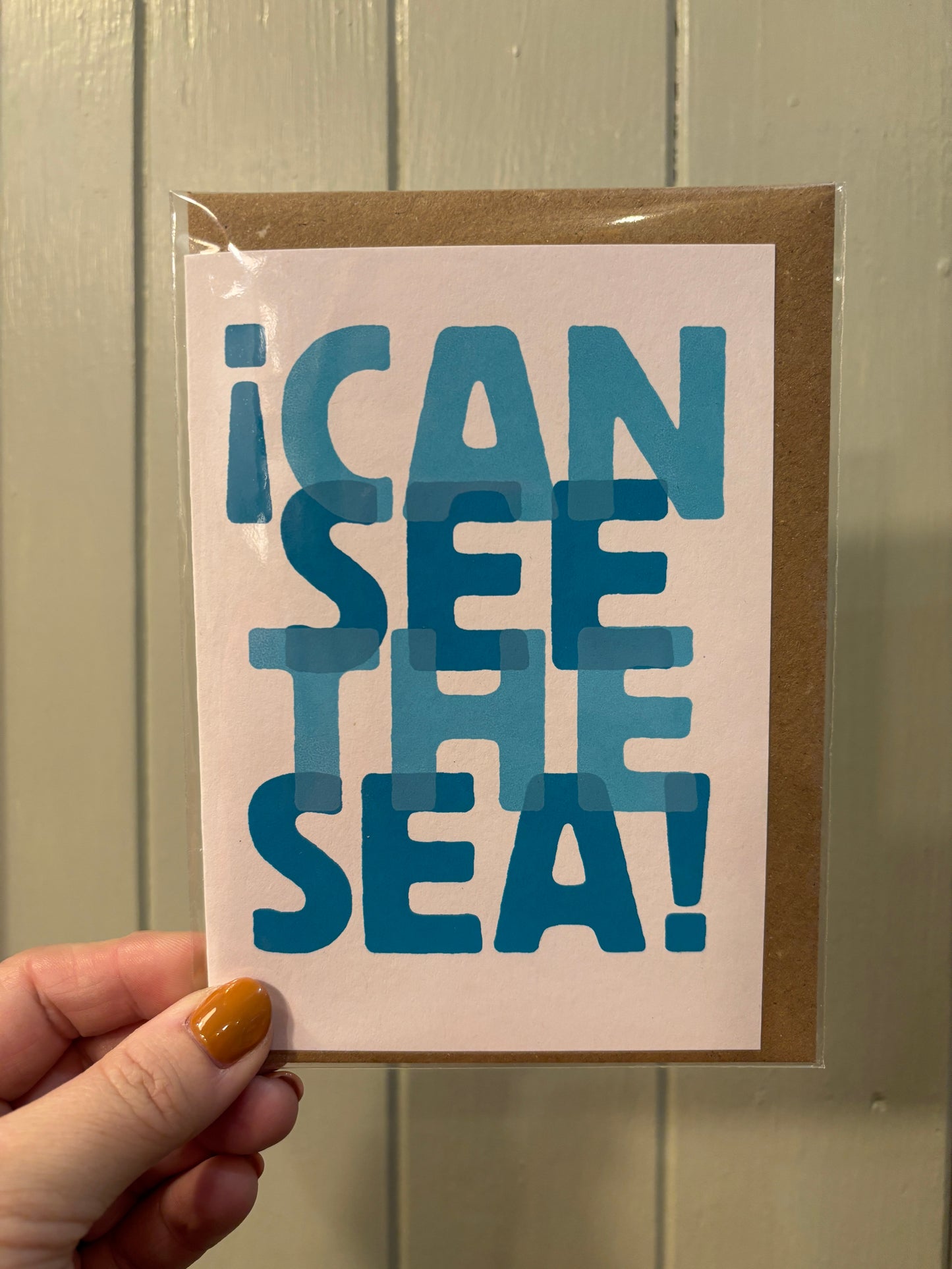 “I Can See the Sea” greeting card—layered blue text on pink, playful coastal stationery for beach lovers