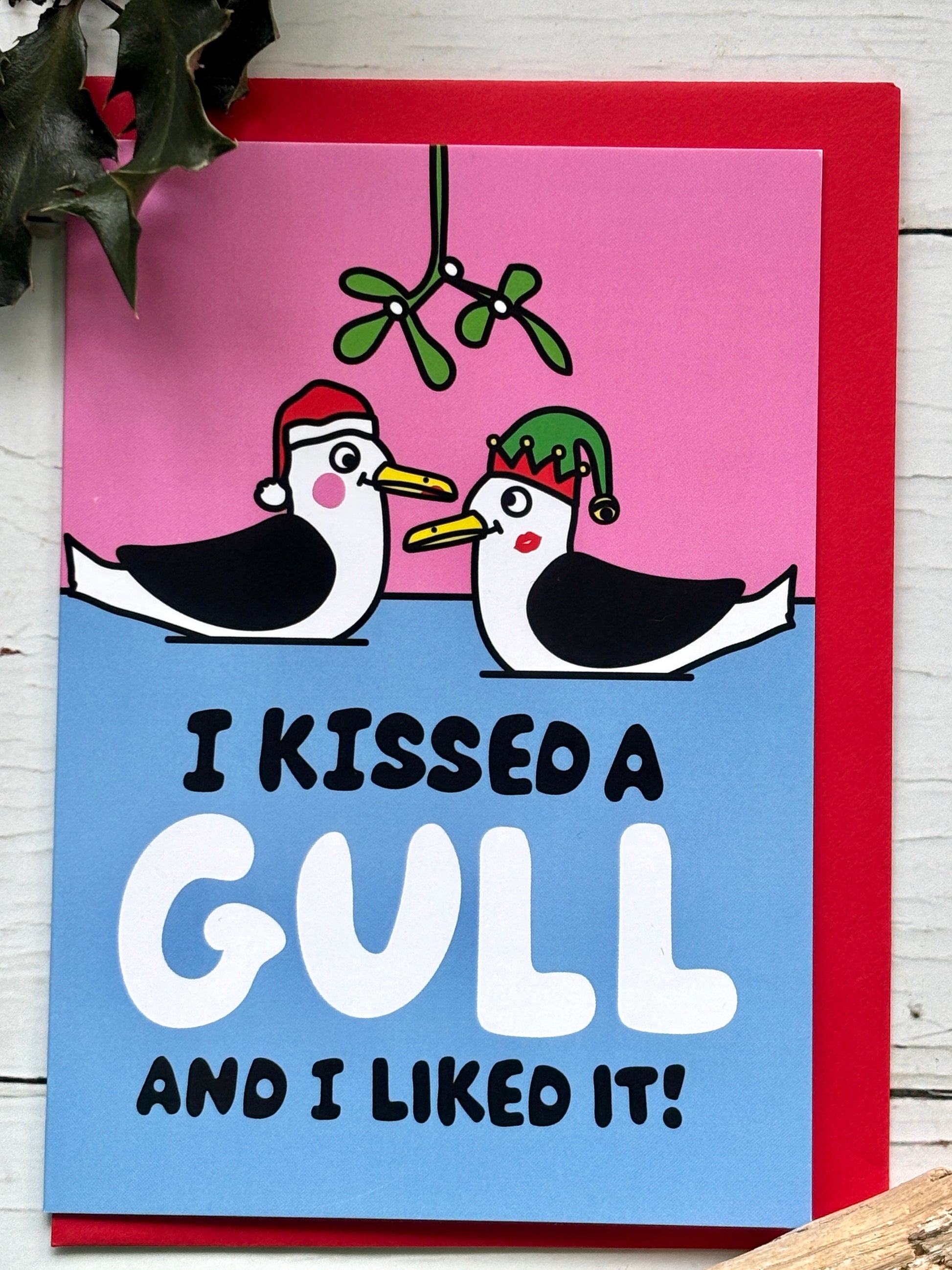 humorous Christmas card lifestyle shot with kissing gulls under mistletoe, quirky coastal illustration, fun festive greeting card