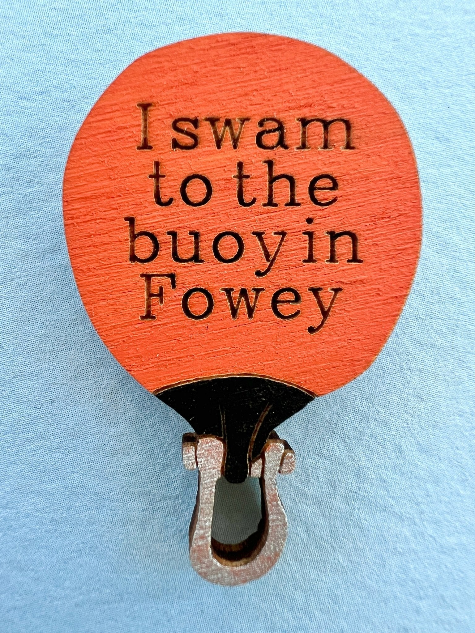 closeup shot of orange buoy-shaped wooden pin badge with “I swam to the buoy in Fowey”—handmade coastal achievement gift