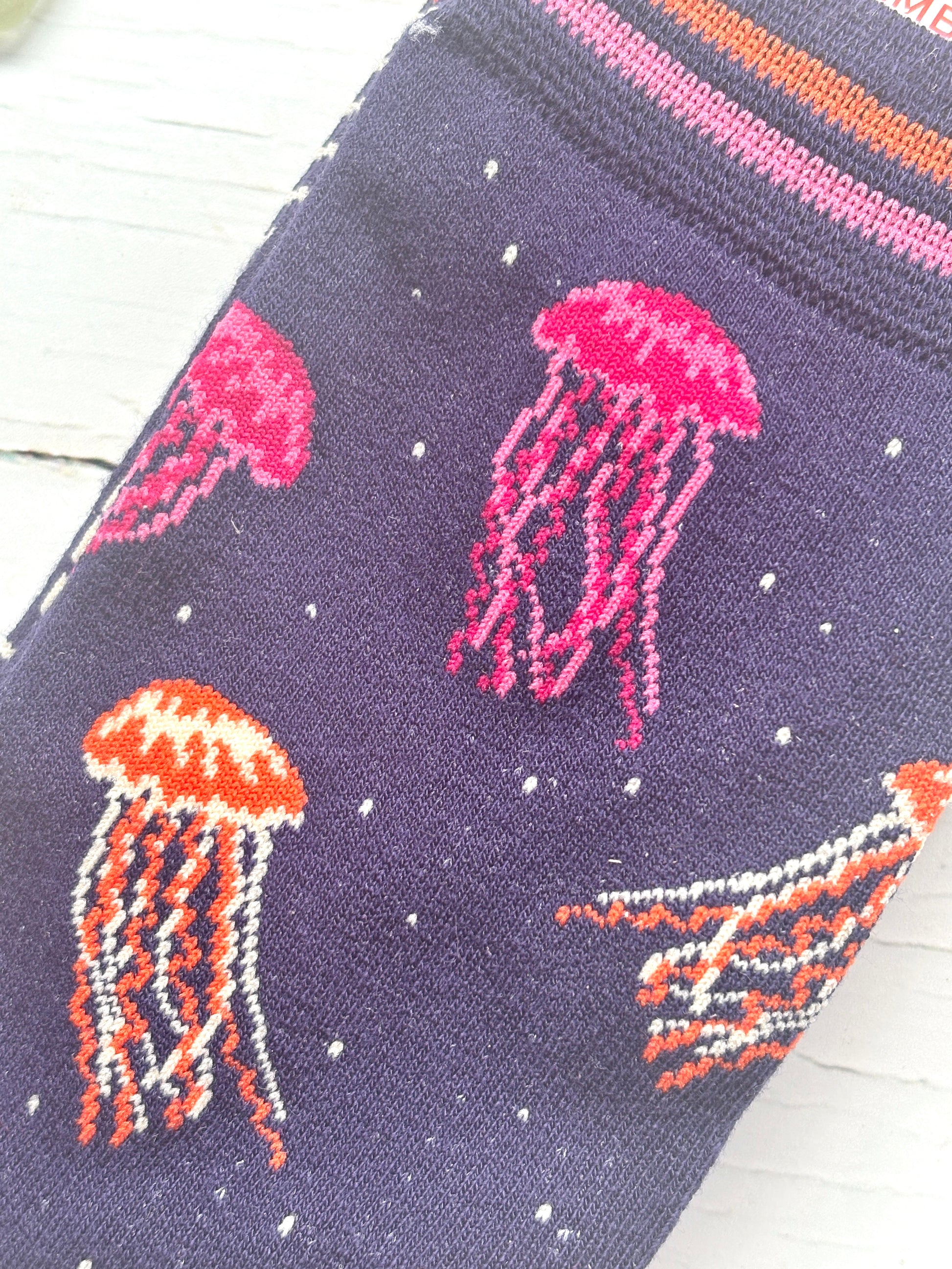 closeup shot of a knitted jellyfish pattern on bamboo socks navy blue background with bright pink and orange sea life design novelty gift