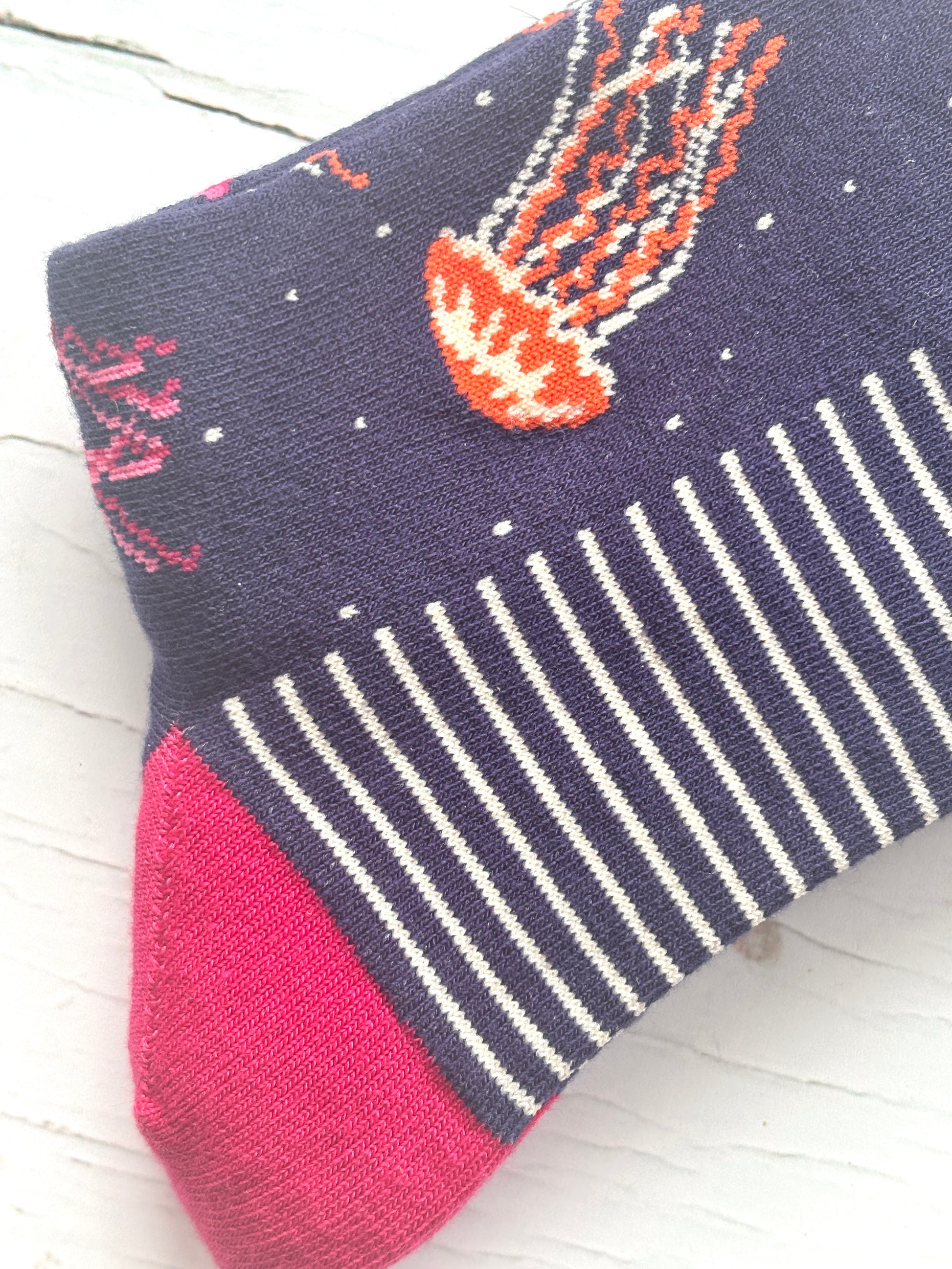 close-up of a navy sock with a striped white cuff, pink toe, and a knitted orange jellyfish bamboo coastal apparel