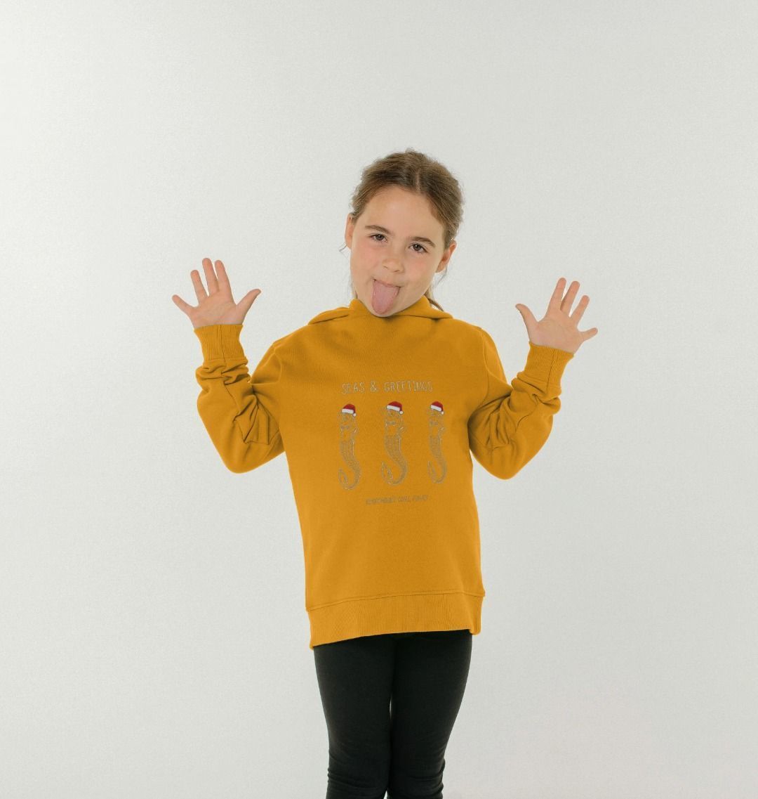kids mustard mermaid Christmas hoodie on child model, “Seas & Greetings” print, cosy festive sweatshirt for winter outfits