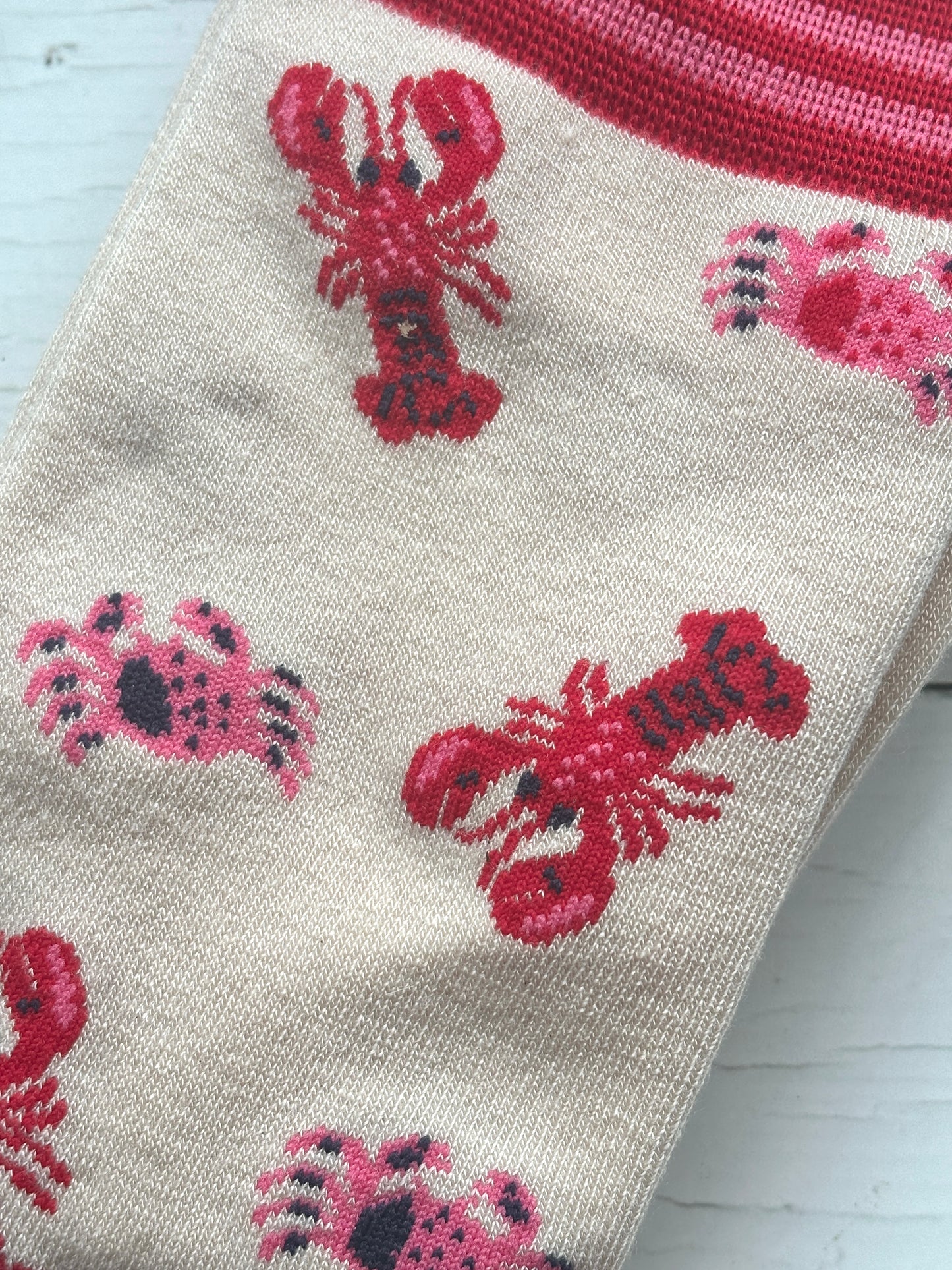 closeup shot of knit pattern of bamboo socks featuring alternating red lobsters and pink crabs unique coastal apparel and sea life gift