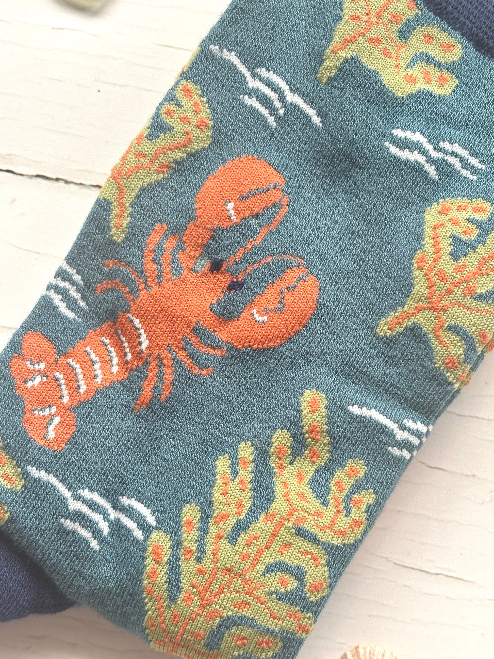 closeup shot of knit pattern of teal bamboo socks featuring a knitted orange lobster and olive green seaweed unique nautical apparel for men