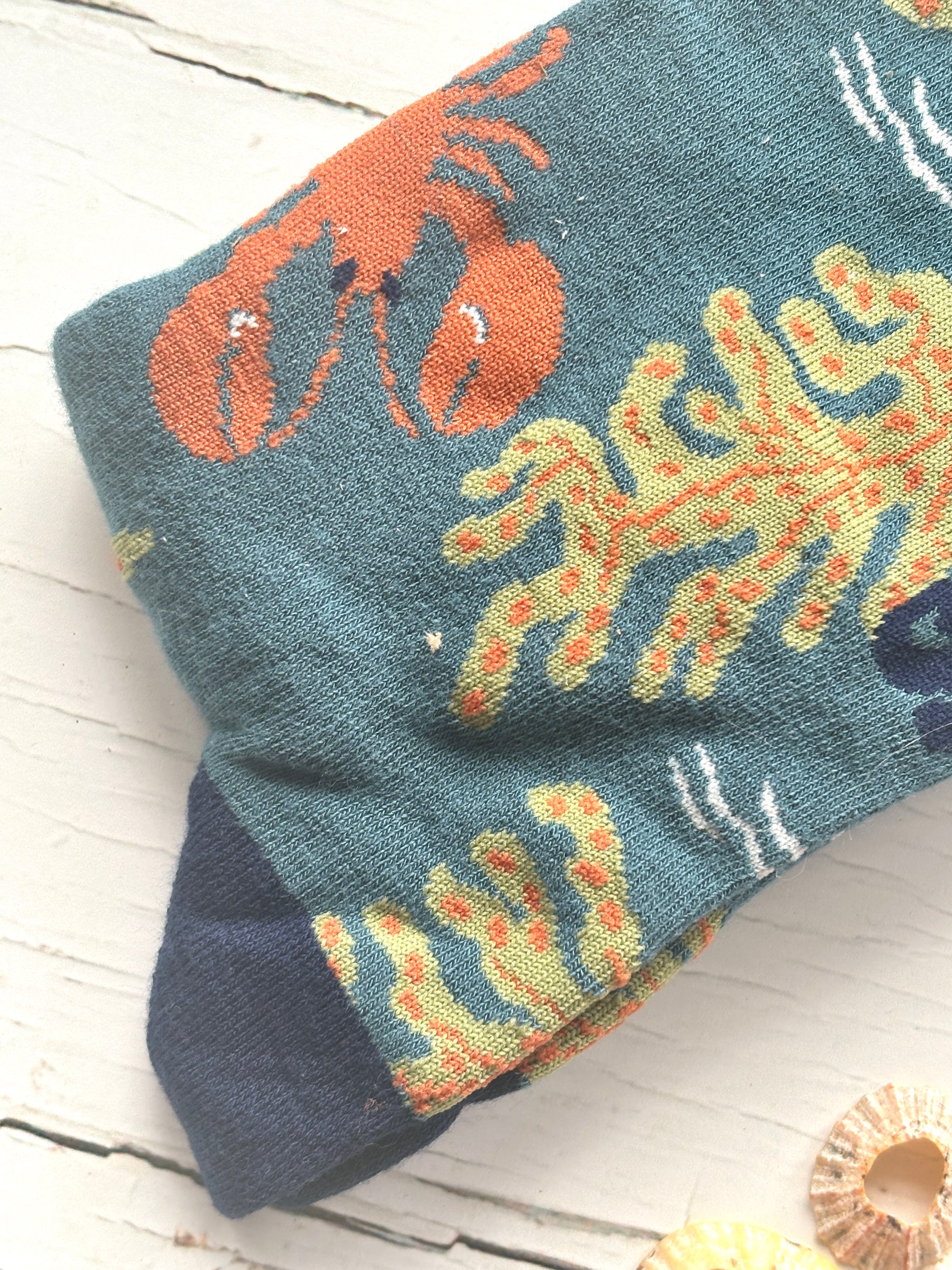 closeup shot of a teal bamboo sock featuring knitted orange lobster and seaweed navy blue toe detail unique coastal gift for men