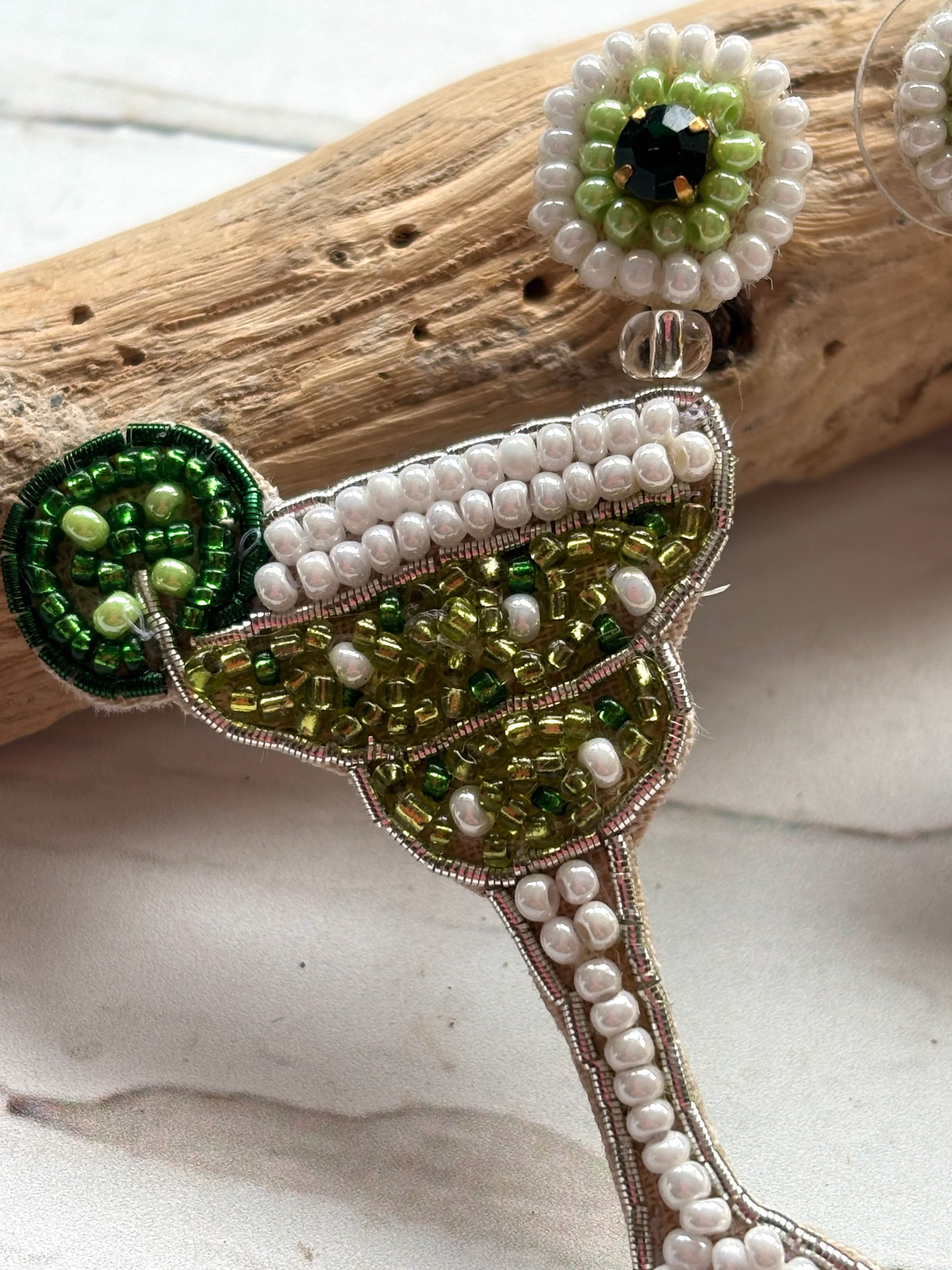 closeup shot of hand-beaded margarita statement earring green & white seed beads detail the cocktail, lime slice, and flower post unique fashion jewelry