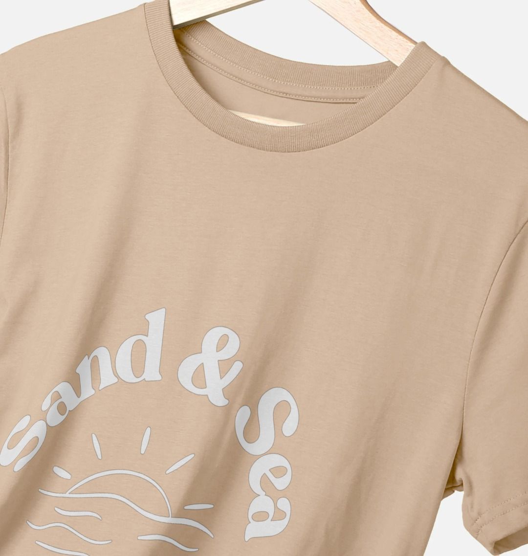 closeup shot of sand-colored T-shirt with white "Sand & Sea" graphic features sun and wave detail men's casual coastal apparel and eco-friendly tee