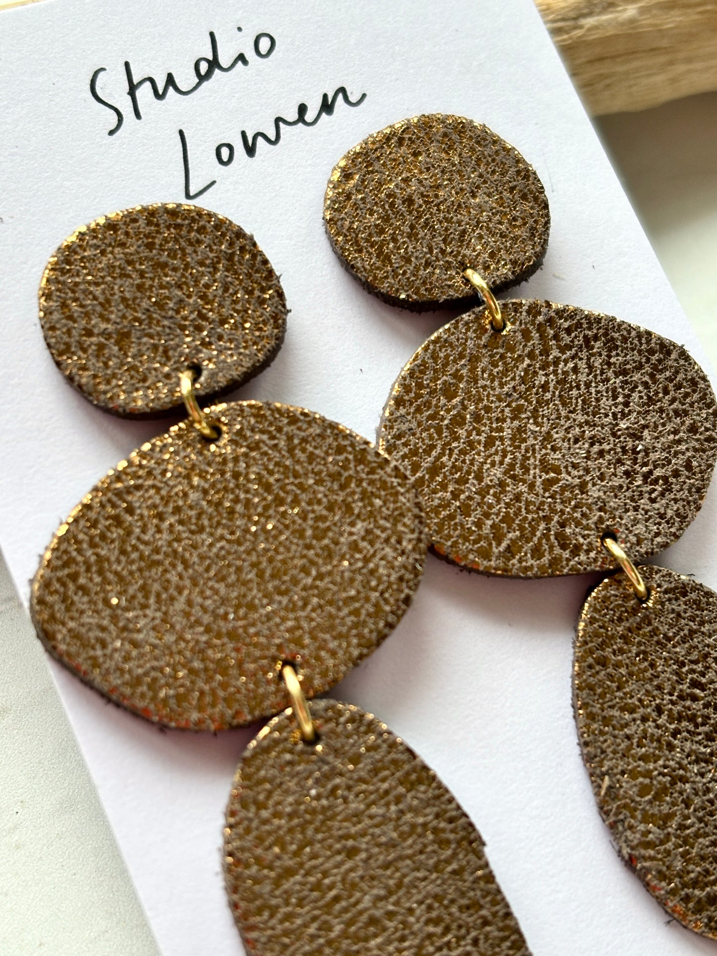 closeup shot of triple metallic bronze leatherette dangle earrings textured statement fashion jewelry with gold links