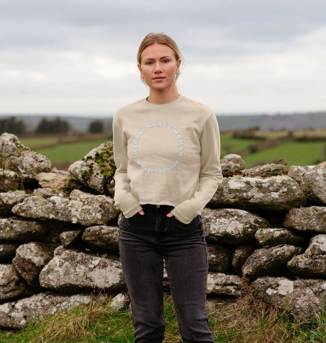 oat middle class woman sweatshirt countryside setting, relaxed fit graphic top, casual outdoor fashion, stone wall backdrop