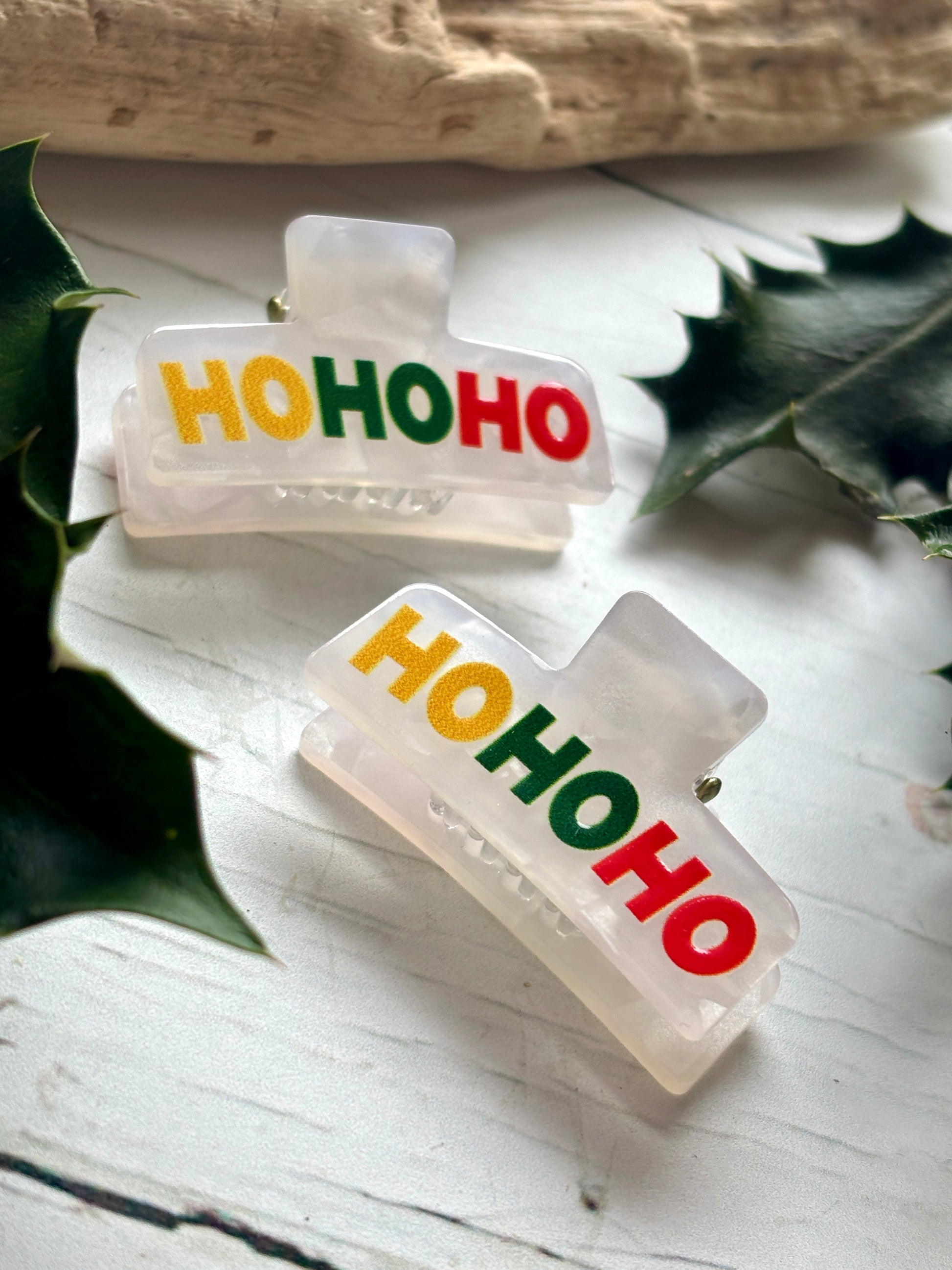 closeup shot of two mini 'HO HO HO' hair claws small acrylic clips with red, green, and gold holiday text festive hair accessories