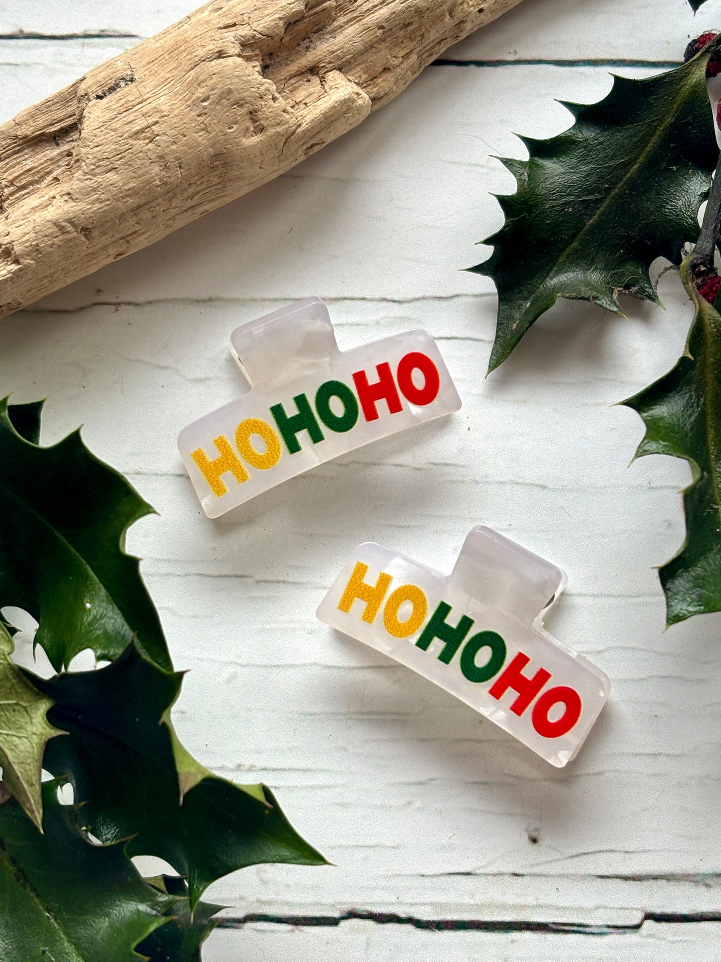 pair of mini white Christmas hair claws. Feature 'HO HO HO' text in yellow, green, and red small festive novelty hair accessories