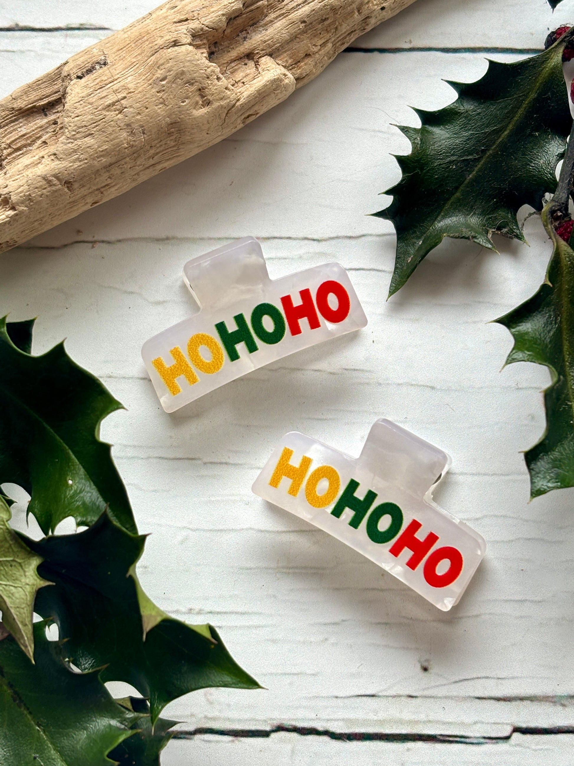 pair of mini white Christmas hair claws. Feature 'HO HO HO' text in yellow, green, and red small festive novelty hair accessories