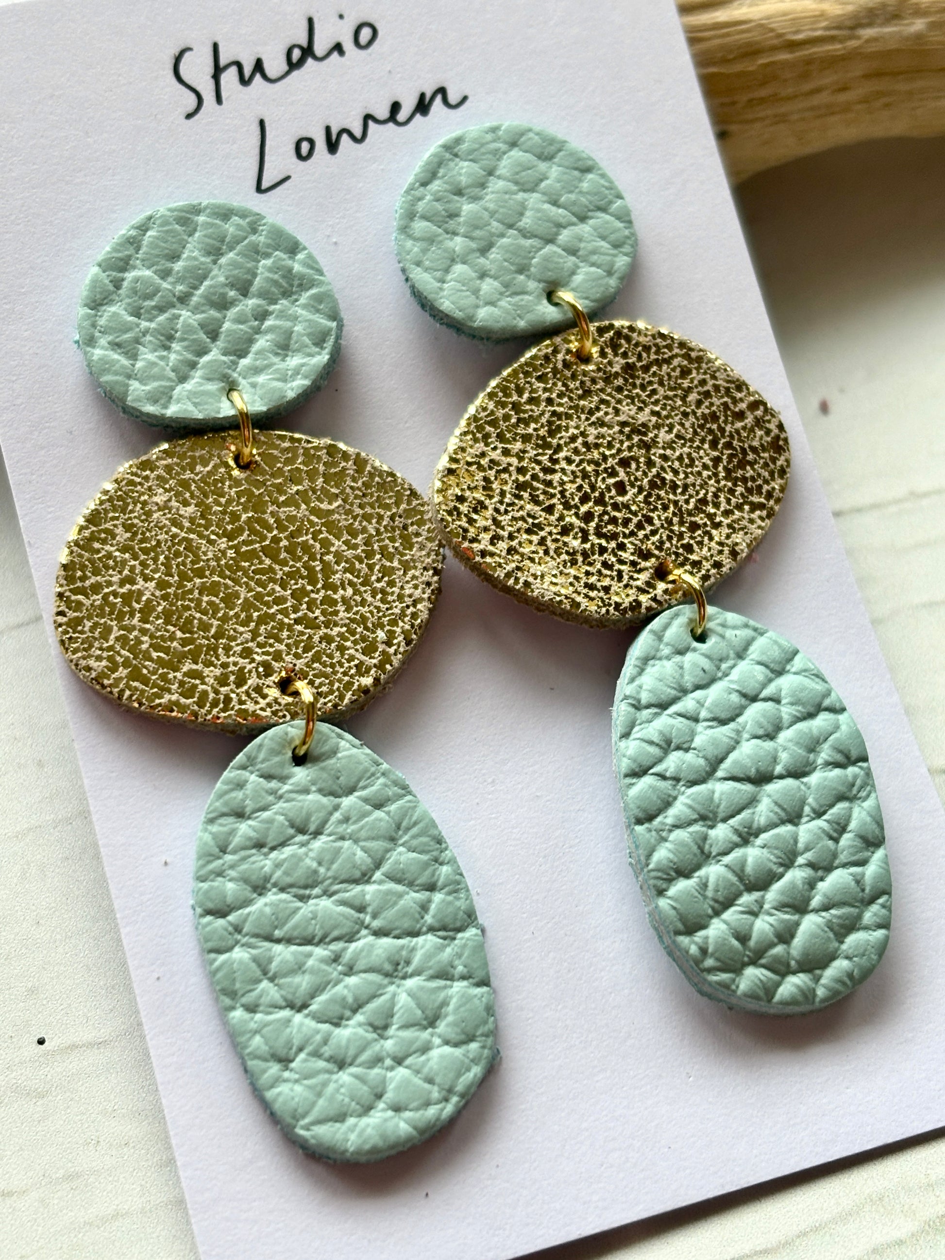 closeup shot of mint green and gold leatherette dangle earrings textured coastal layered statement jewelry with gold links