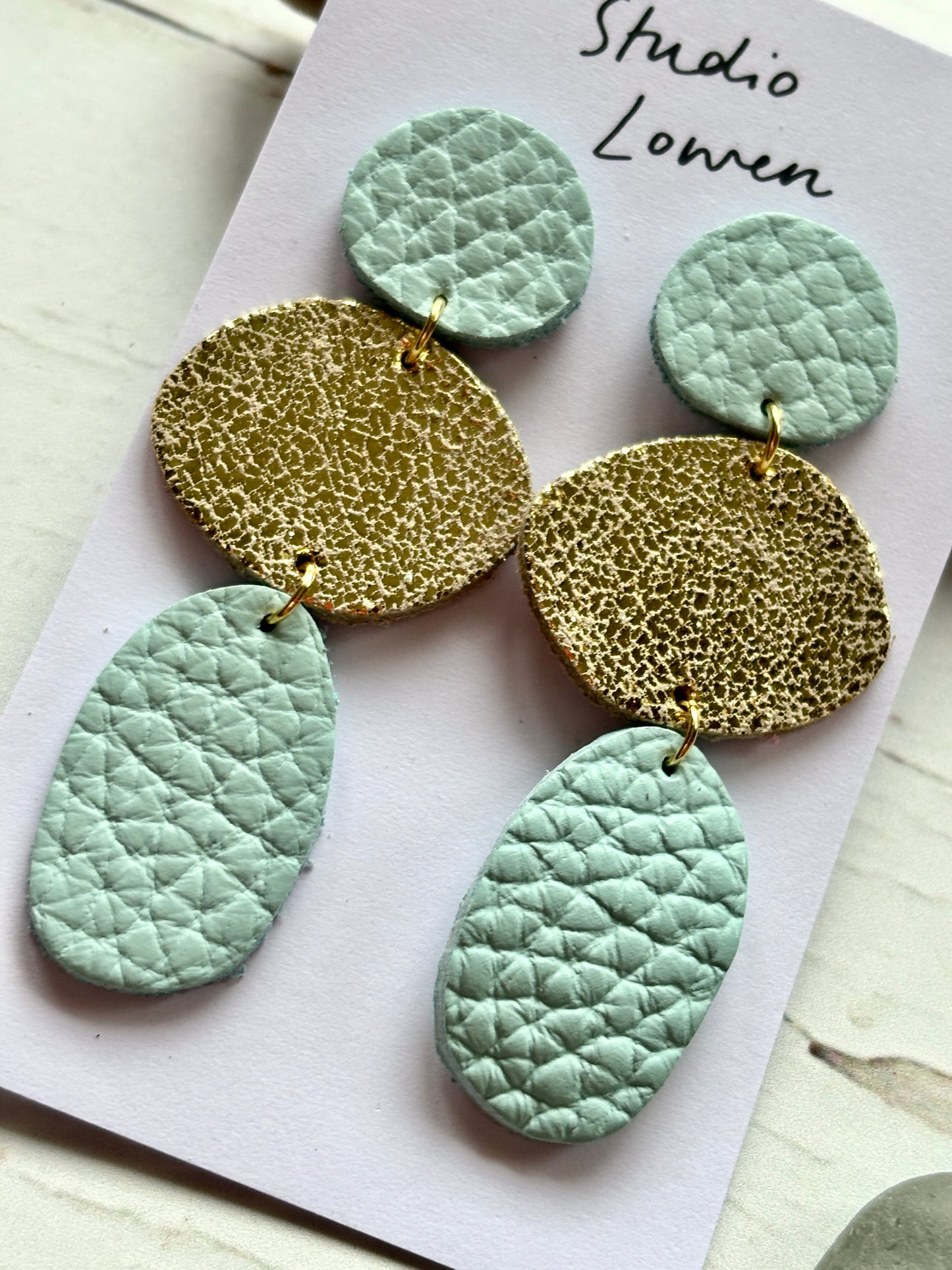 closeup shot of mint and metallic gold triple drop earrings textured coastal layered faux leather statement jewelry