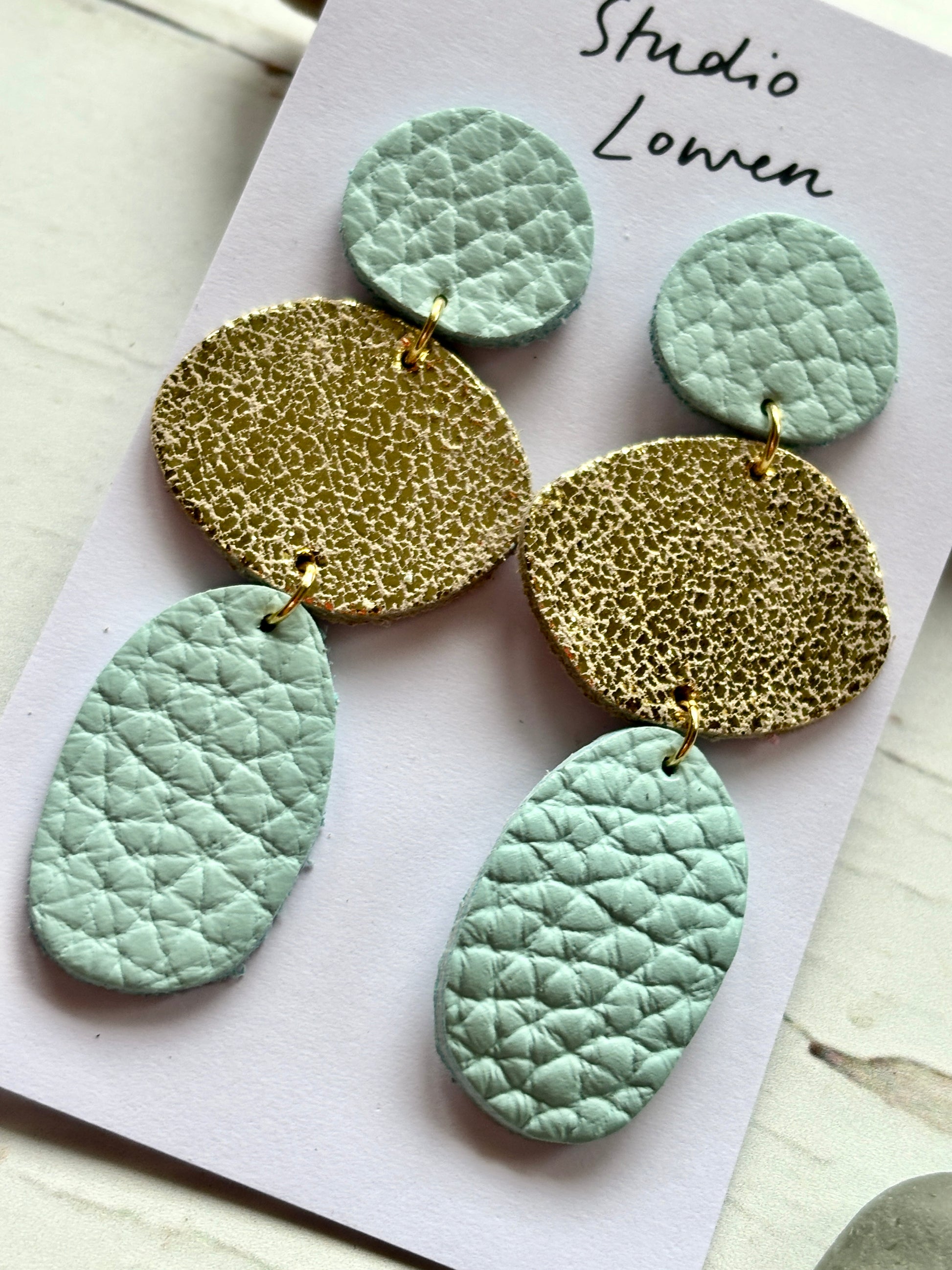 closeup shot of mint and metallic gold triple drop earrings textured coastal layered faux leather statement jewelry