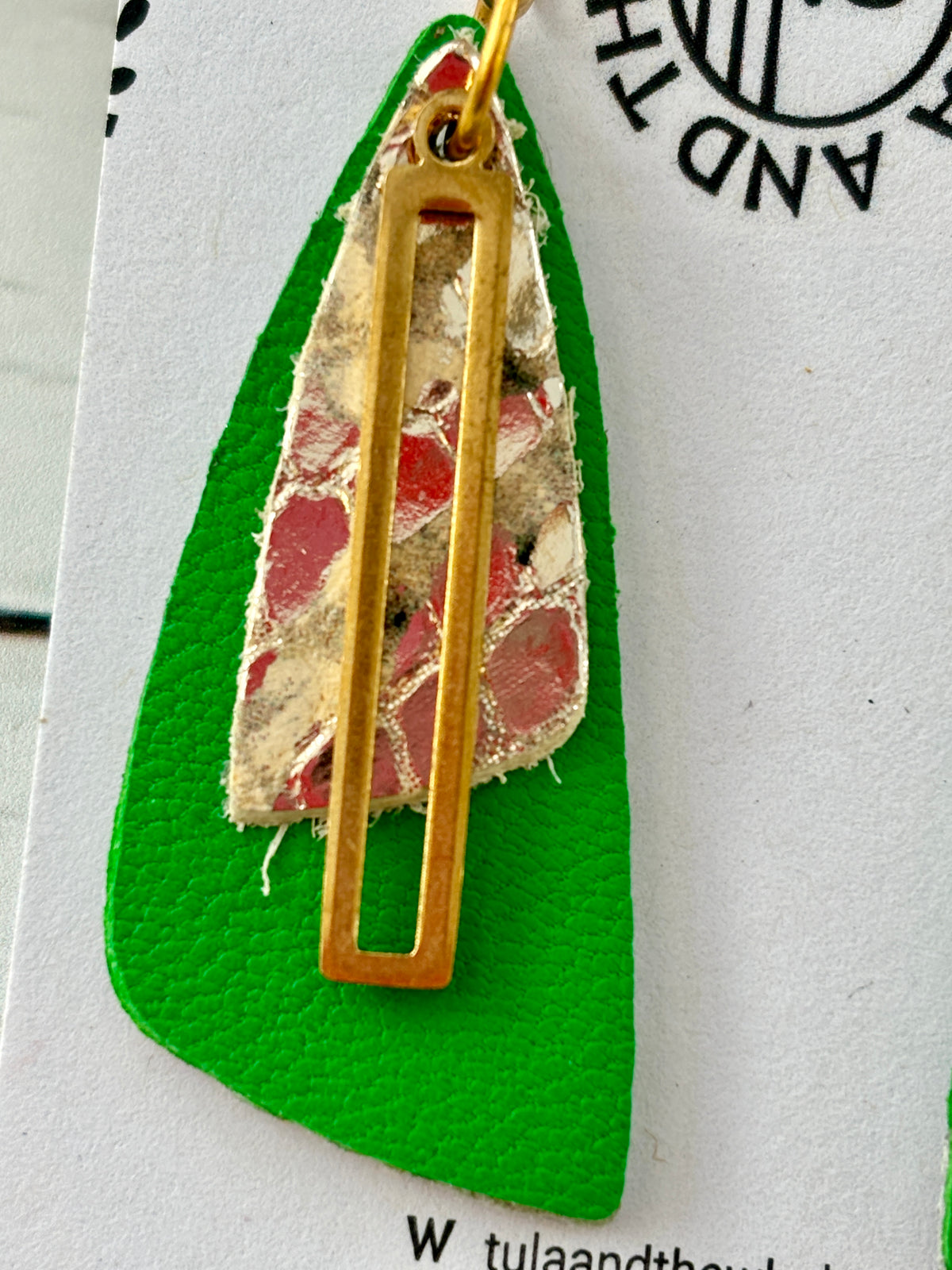closeup shot of handmade green leather earrings with gold snake-textured layer and cut-out accent—bold statement jewelry