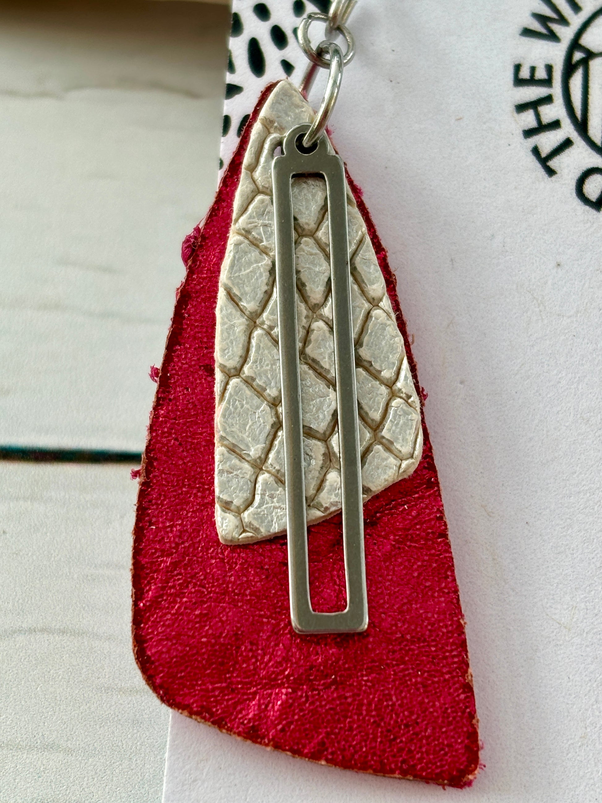 closeup shot of handmade earrings with metallic pink leather, silver snakeskin texture, and gold accent—bold statement jewelry