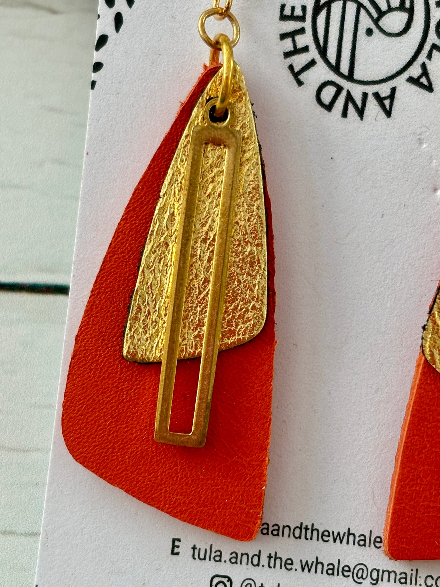 closeup shot of handmade orange and gold leather earrings with geometric moth-wing design—bold, lightweight statement jewelry