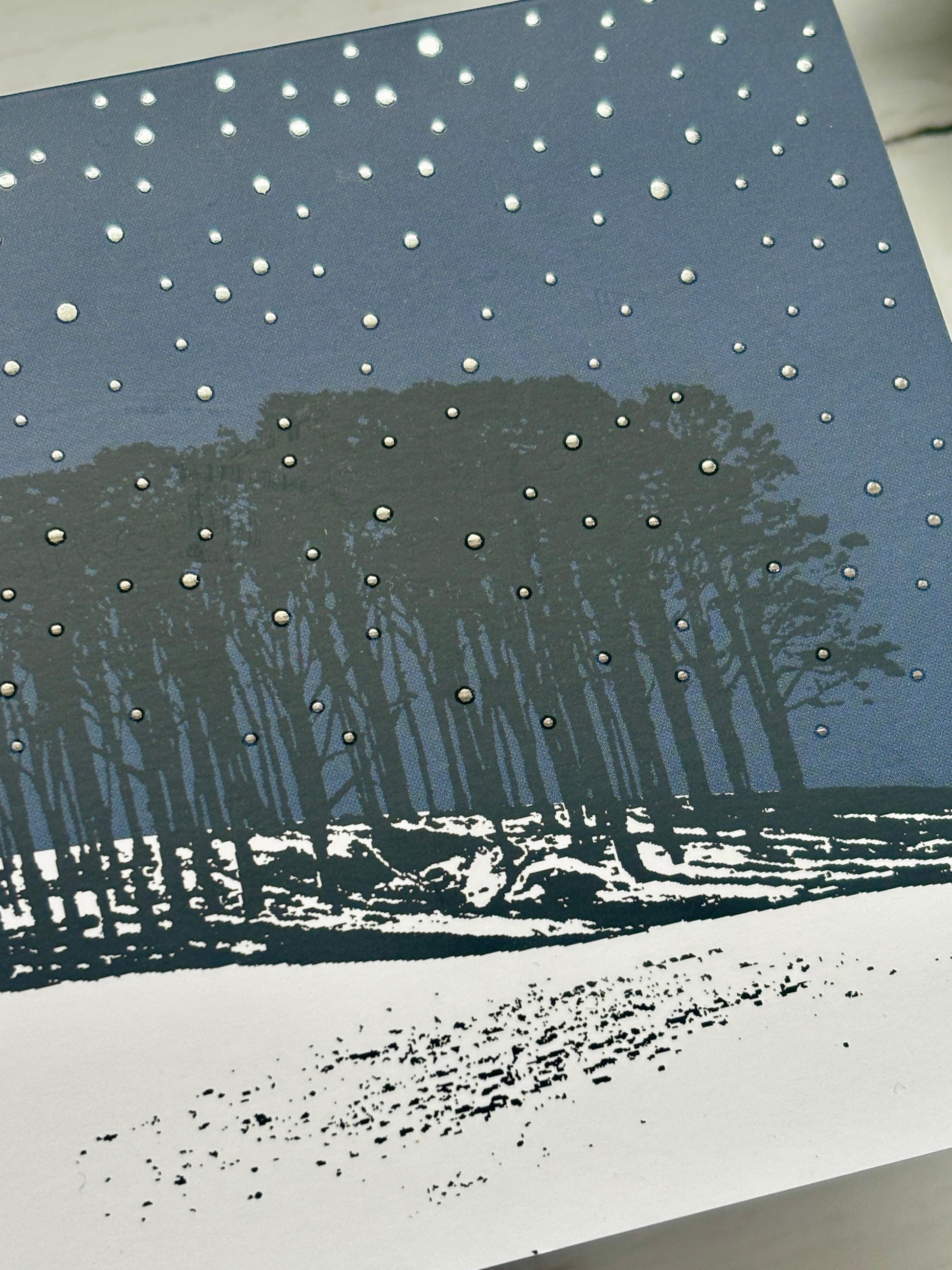 closeup shot of winter Christmas card with snowy hill, pine trees, and metallic starry sky, festive woodland holiday design