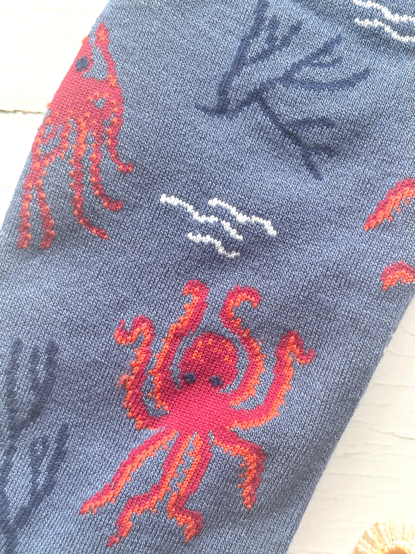 closeup shot of bamboo sock knit red octopus, blue seaweed, and white waves on a slate blue background coastal apparel gift