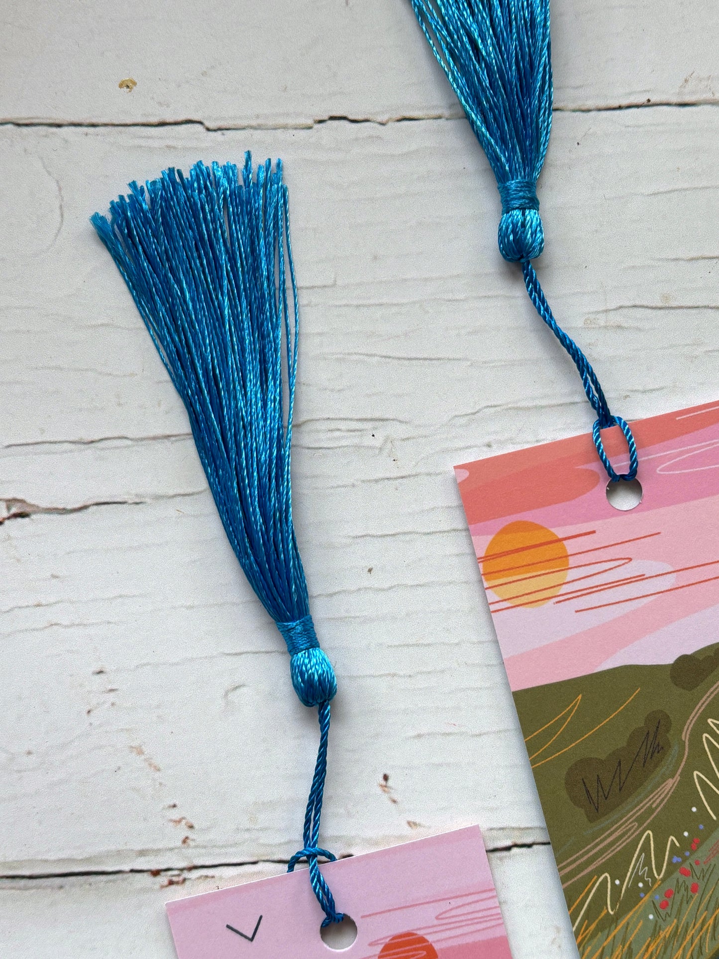 closeup shot of two electric blue tassels silk thread bookmark accessories on a white wooden background handmade reading gift