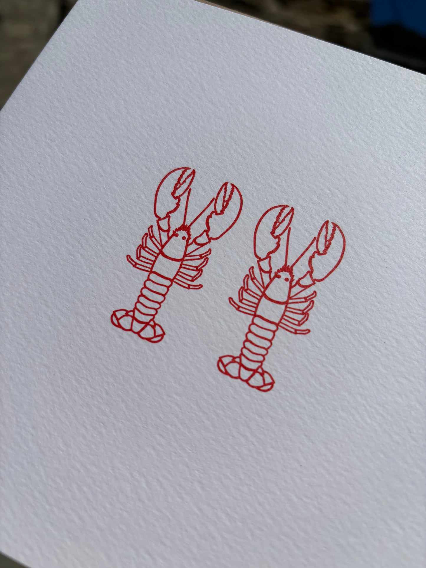 closeup shot of two red lobster drawings up close on textured white card minimalist coastal art for anniversary or a unique love greeting card