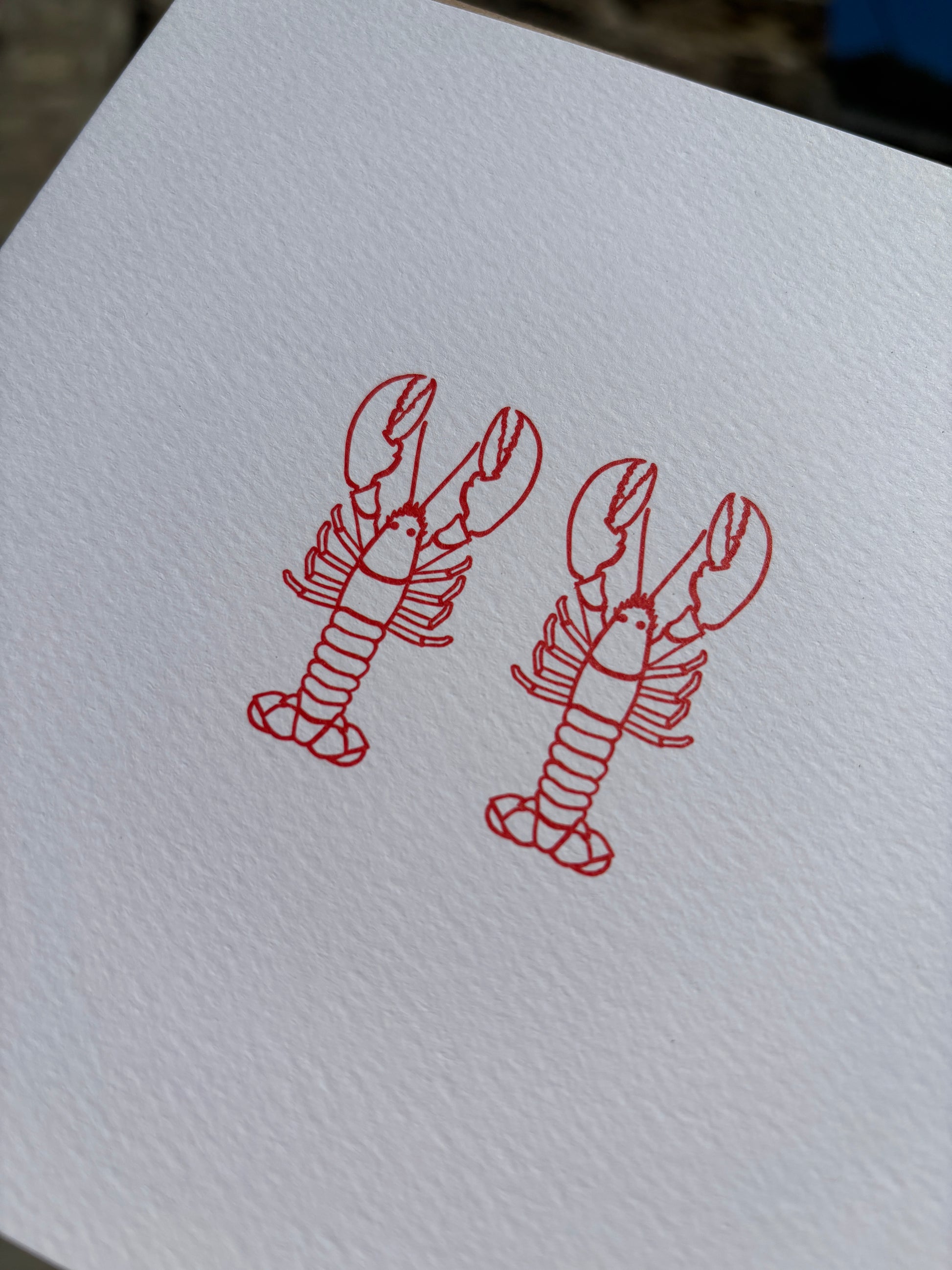 closeup shot of two red lobster drawings up close on textured white card minimalist coastal art for anniversary or a unique love greeting card