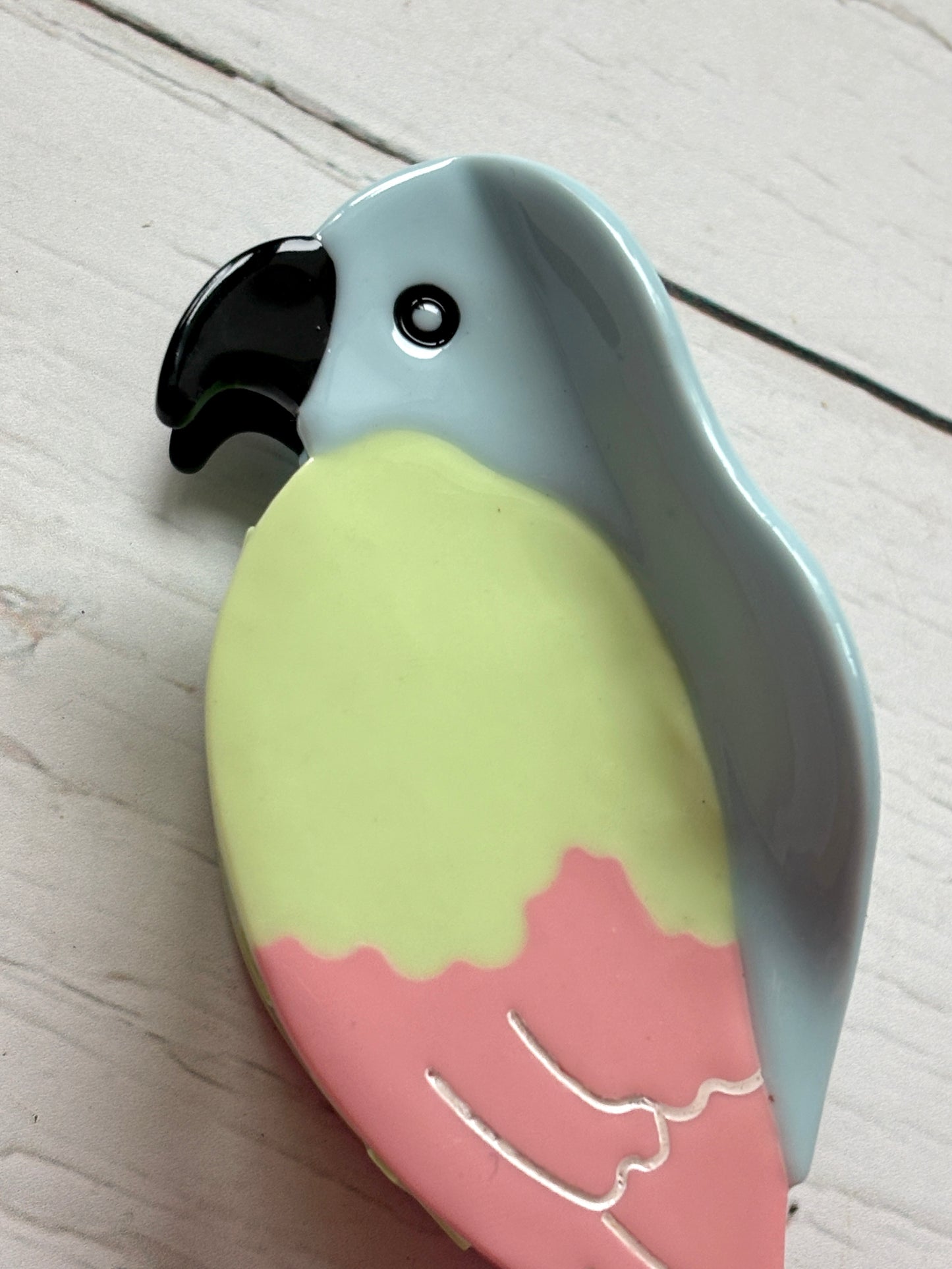 closeup shot of pastel parrot hair claw—glossy multicolor clip with tropical tones, feather detail, and secure grip