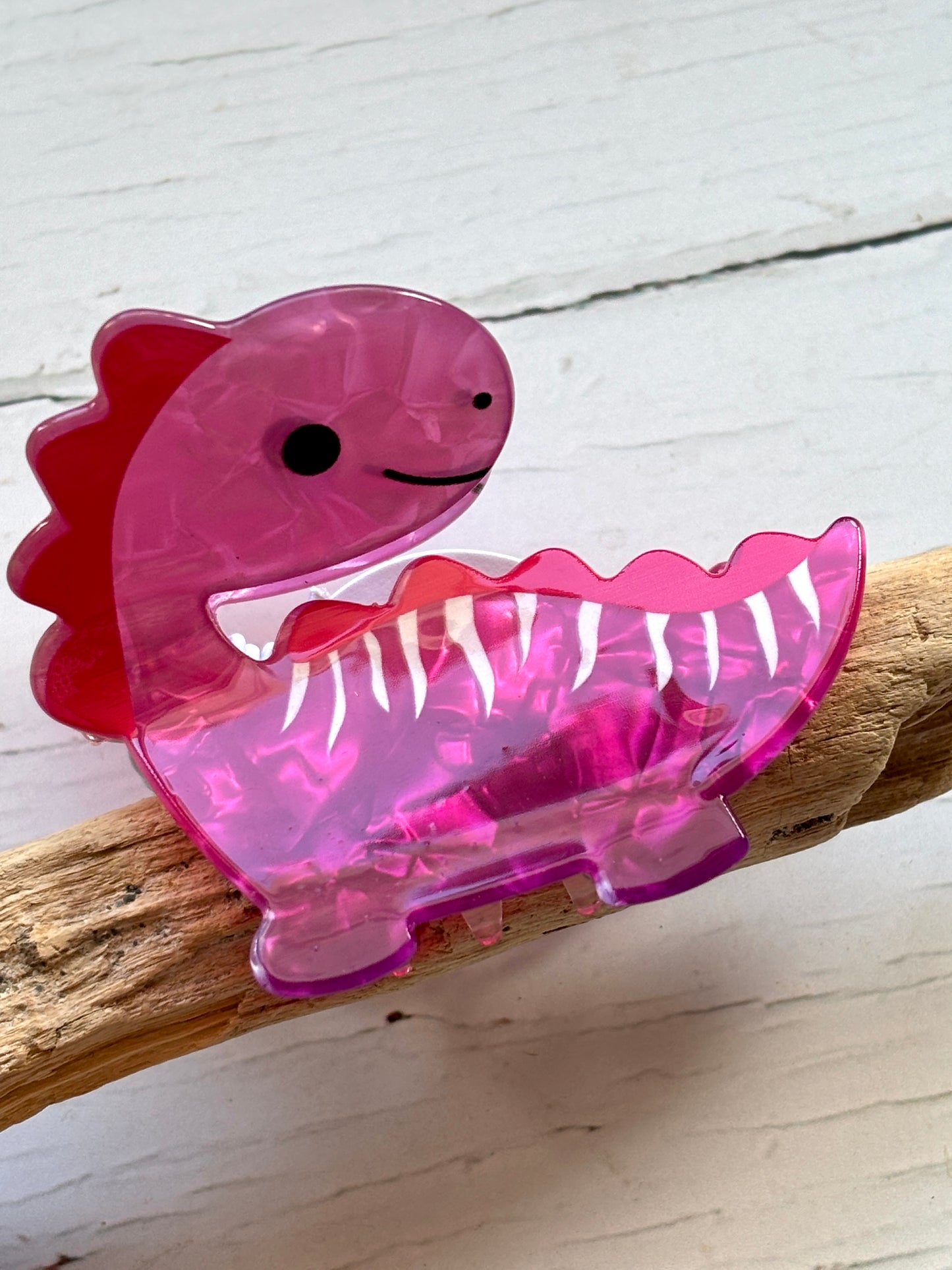 funky pink dinosaur hair claw clip made of marbled acrylic novelty statement hair accessory or cute dino hair decor on driftwood