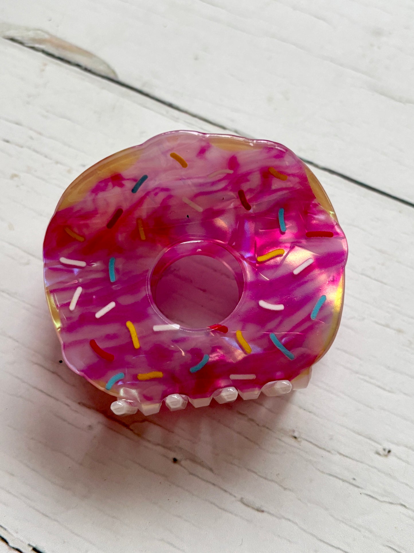 closeup shot top view of the pink doughnut hair claw clip with colorful sprinkles, highlighting the iridescent frosting and teeth