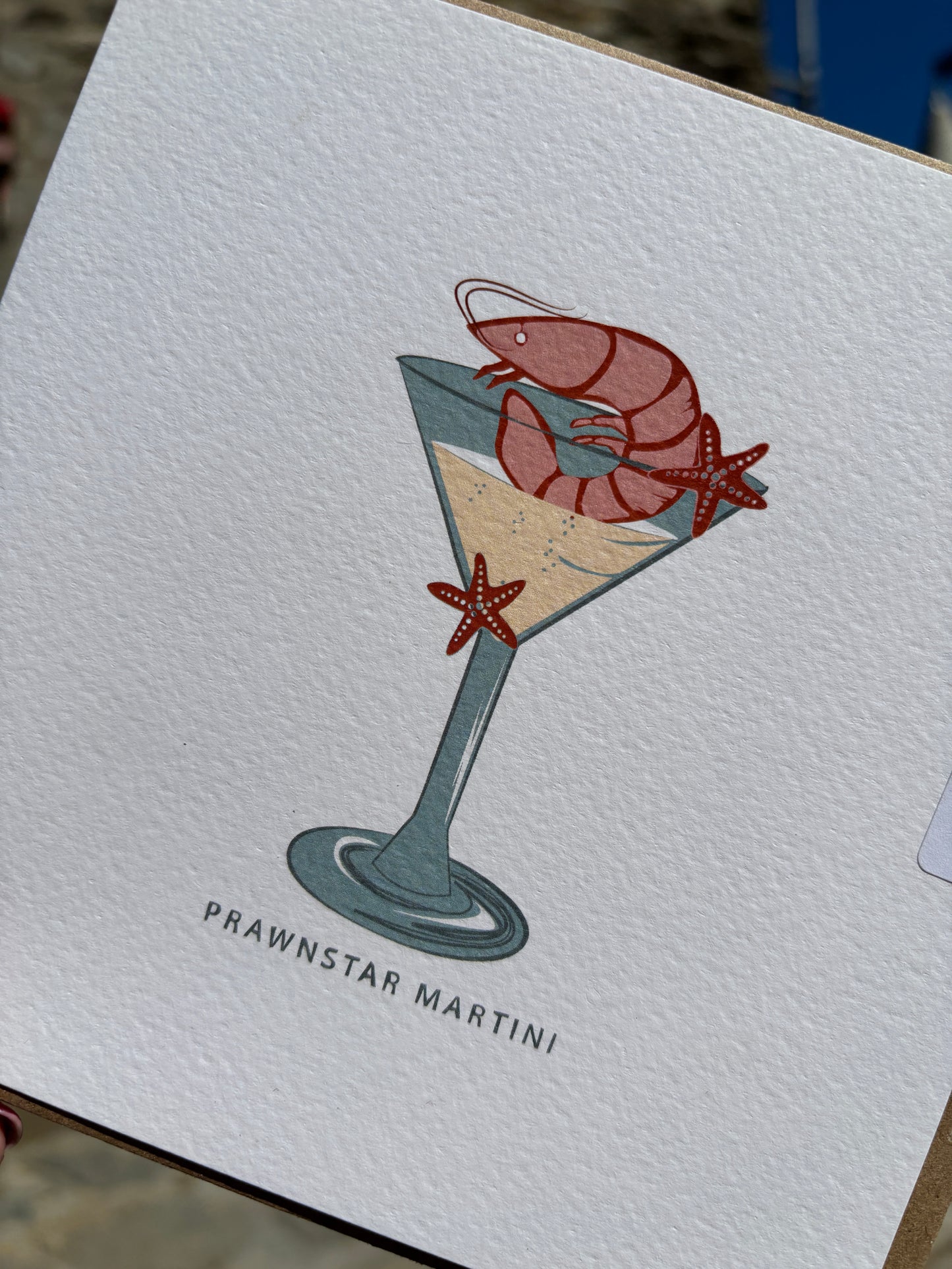 closeup shot of prawnstar Martini greeting card—quirky prawn and starfish cocktail illustration on textured paper, ideal for coastal humor and gifting