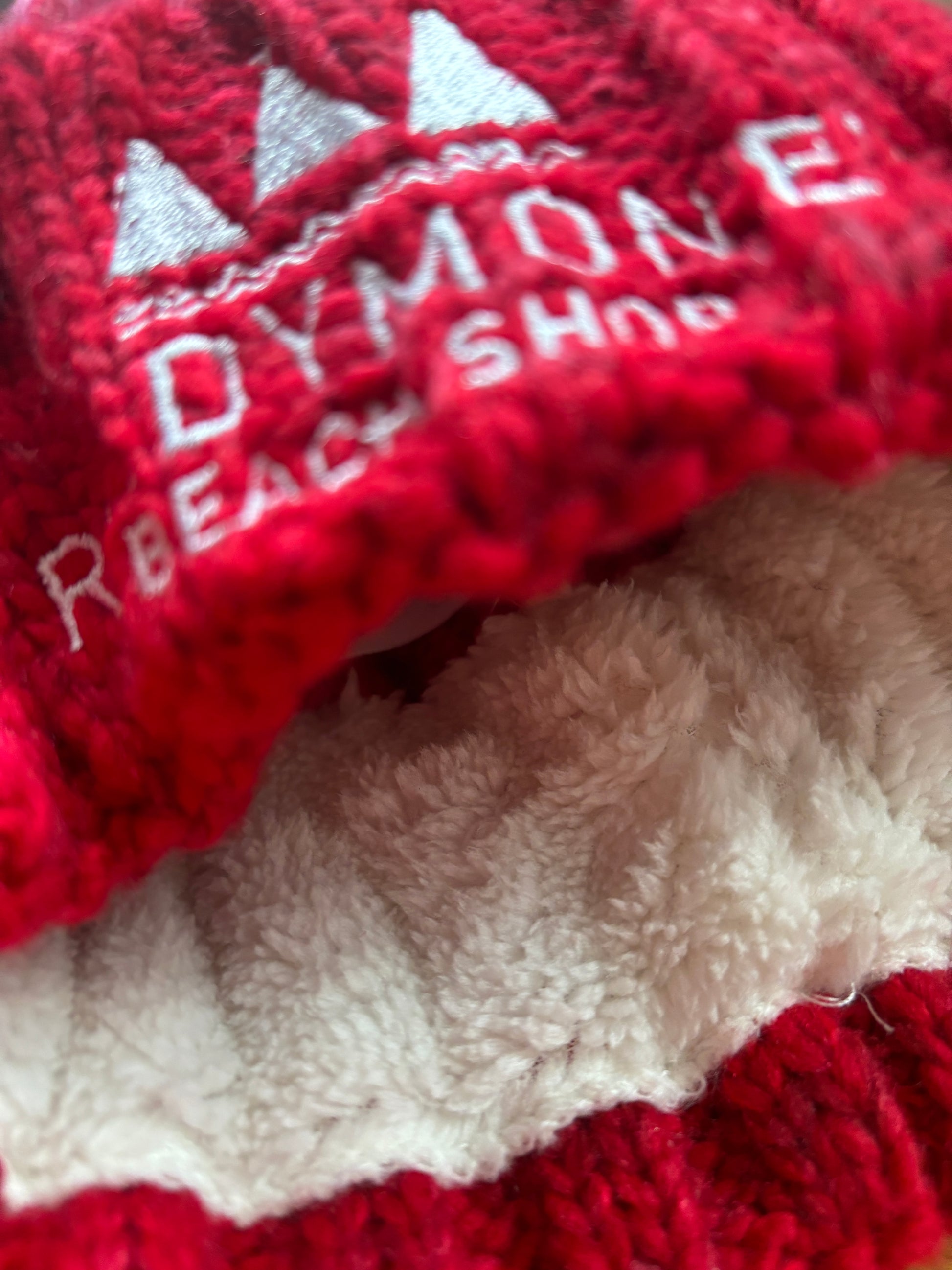 closeup shot of chunky red-white bobble hat with soft fleece lining and beach shop embroidery—cozy, bold, and winter-ready