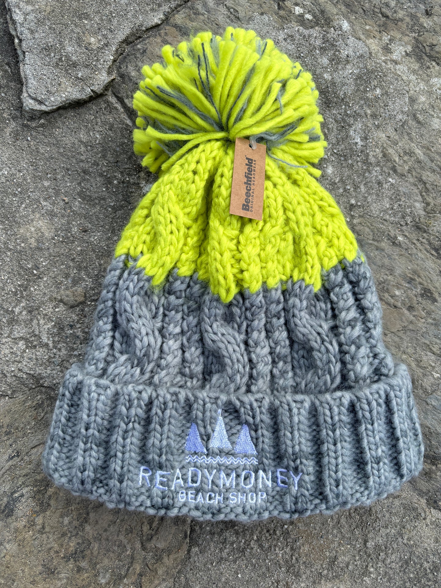 grey-lime chunky bobble hat with faux fur pom-pom and beach shop logo—bold, cozy, and perfect for winter adventures