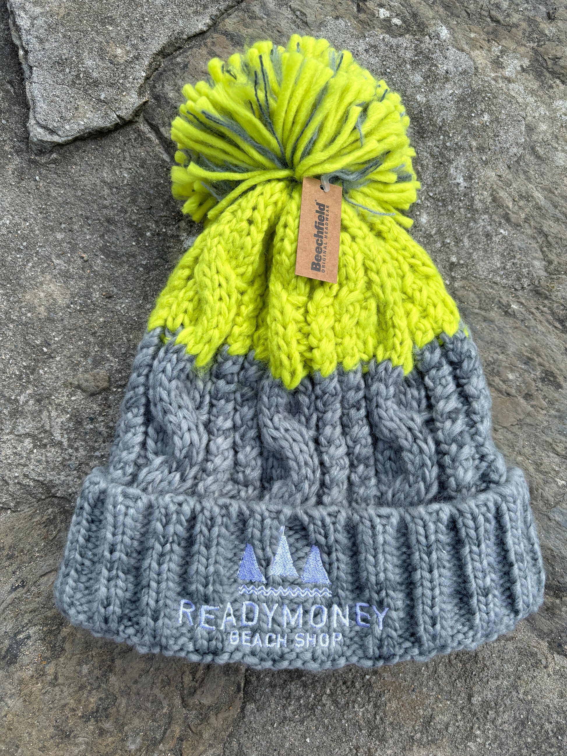 grey-lime chunky bobble hat with faux fur pom-pom and beach shop logo—bold, cozy, and perfect for winter adventures