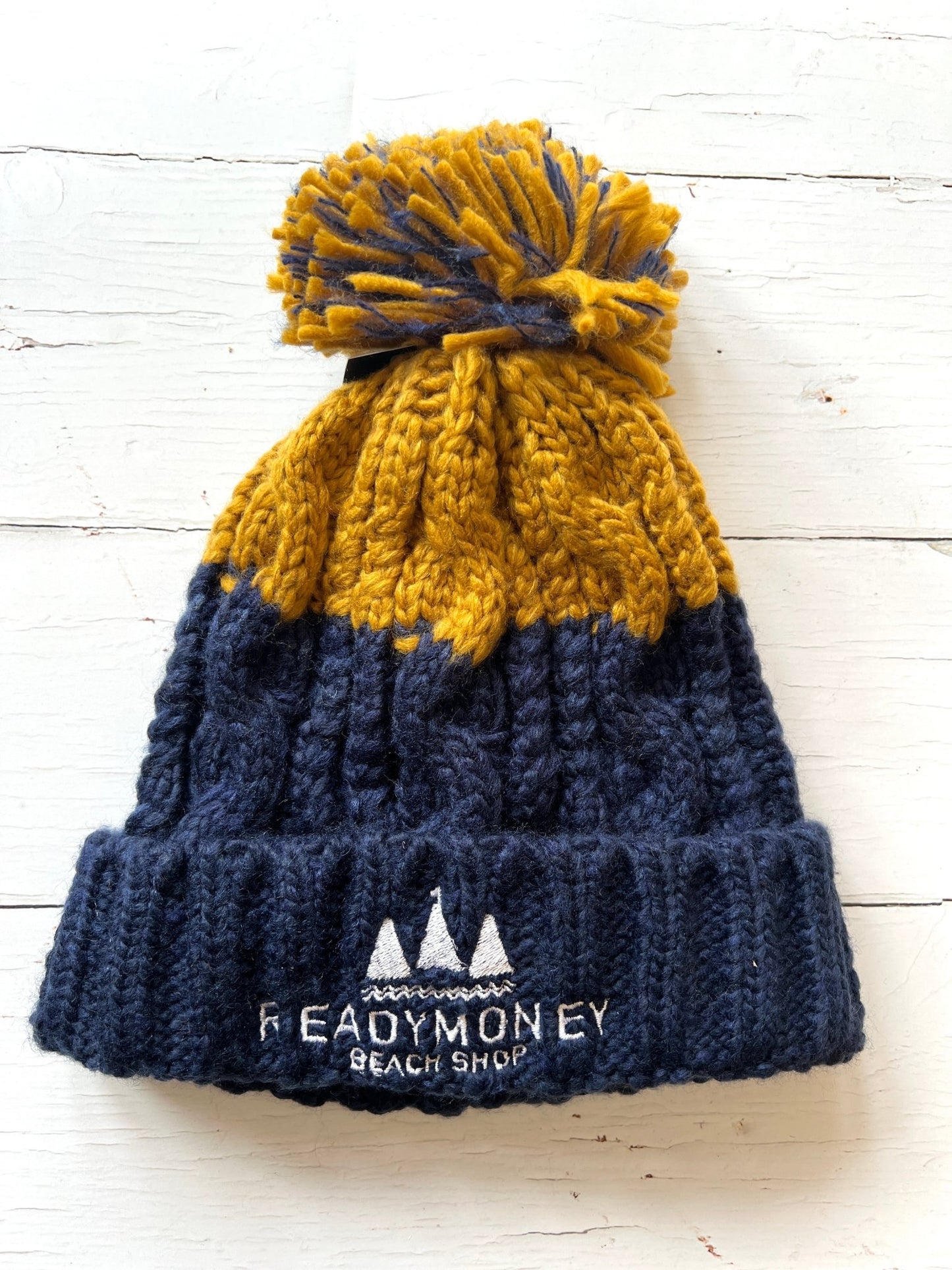 navy-mustard chunky bobble hat with faux fur pom-pom and beach shop logo—warm, bold, and coastal-cool for winter